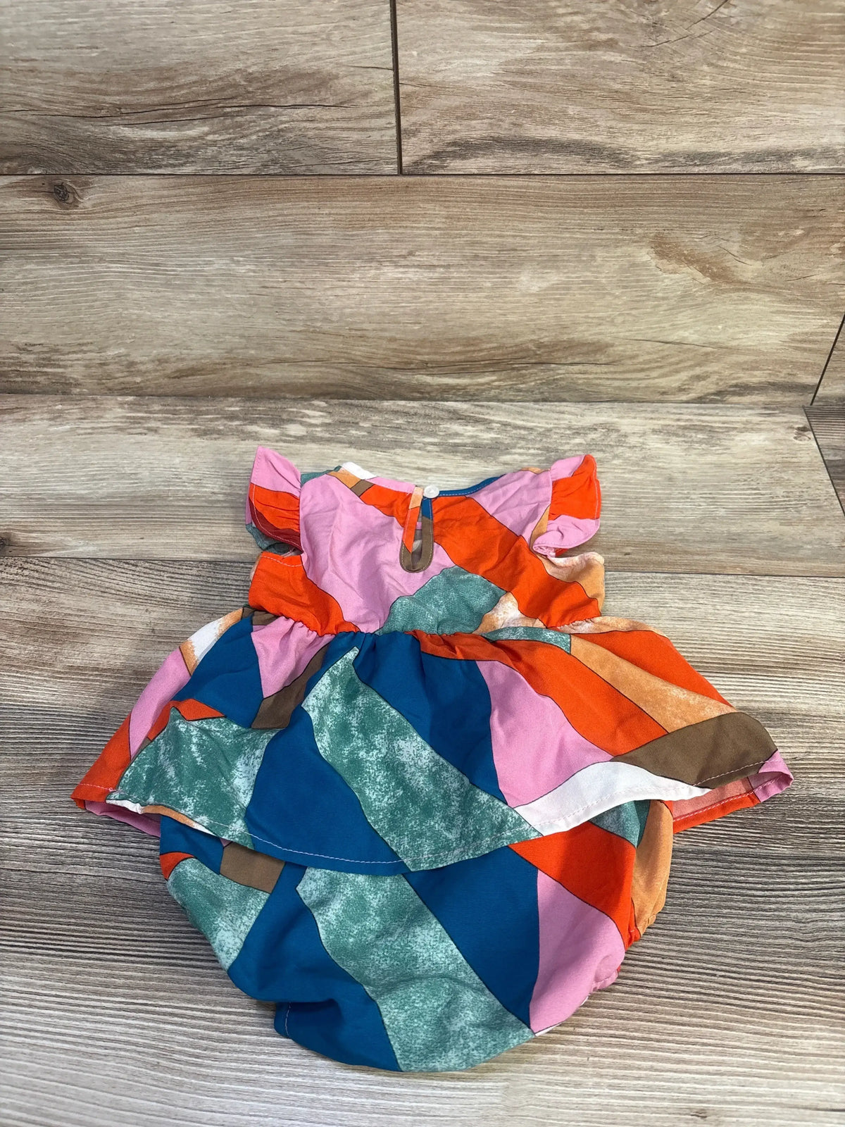 Top-down view of PatPat multicolor bodysuit dress for 6 to 9 months with geometric panels and gathered skirt on wood flooring