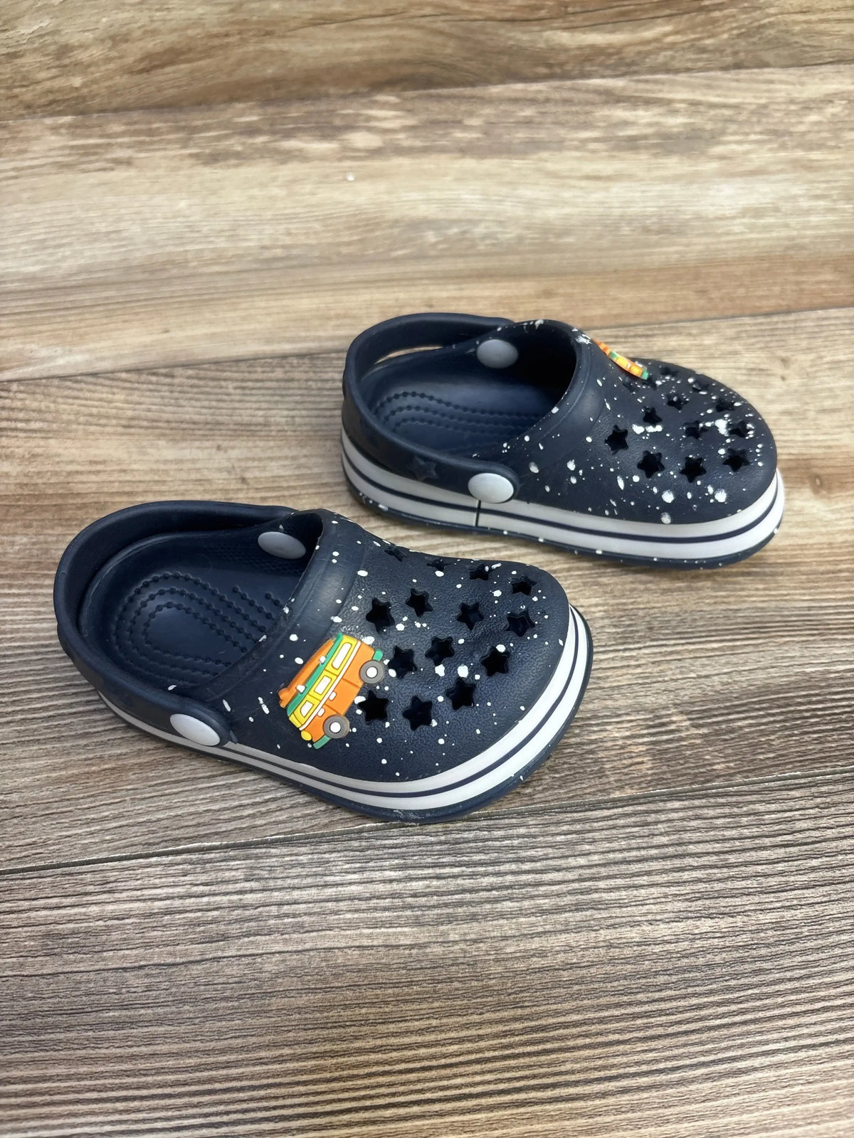 Three-quarter view of Koala Kids blue clogs showcasing star-shaped toe cutouts, white paint-splatter detailing, and orange van charm on wood floor