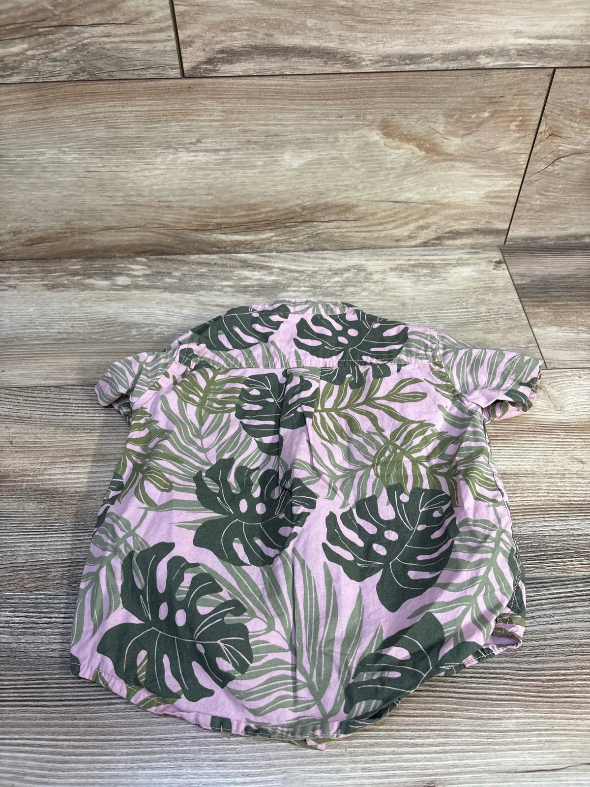 Flat lay back view of pink short sleeve button up shirt with green tropical leaf print on wood floor