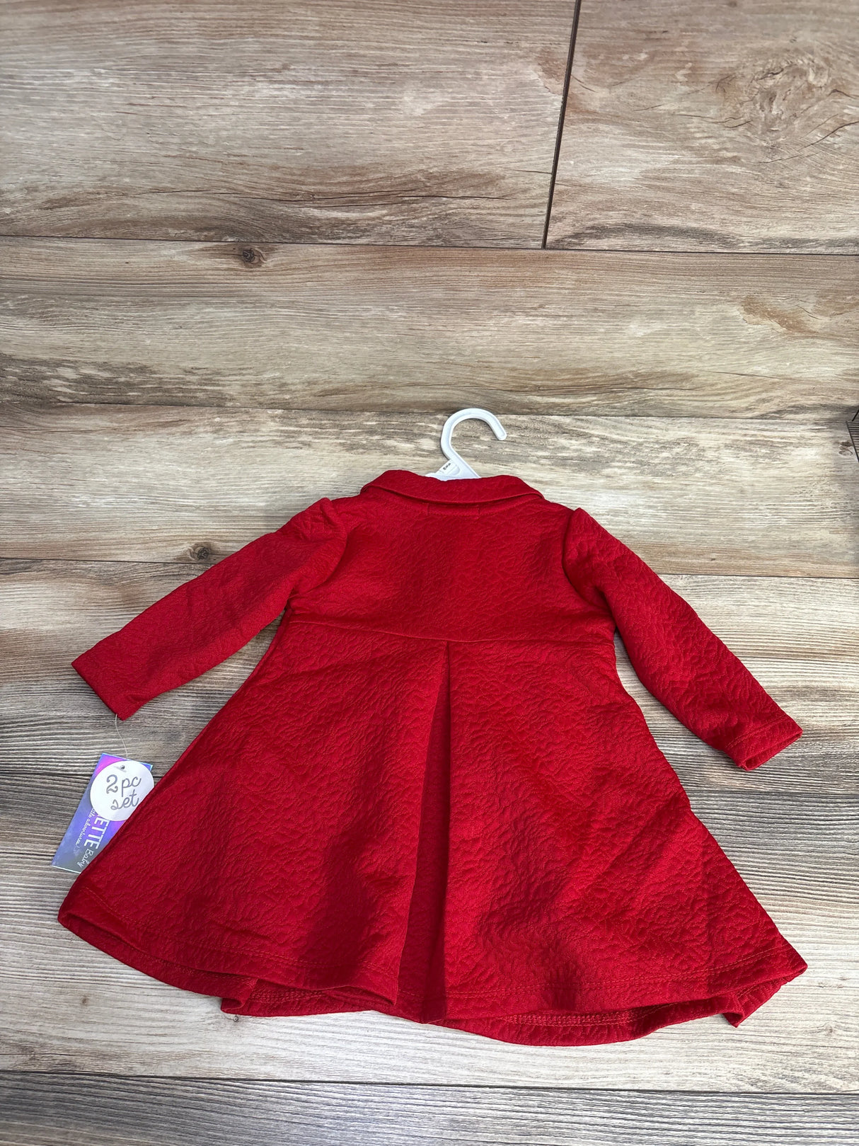 Red textured long-sleeve baby girl's dress on white hanger on wooden floor, kids clothes resale
