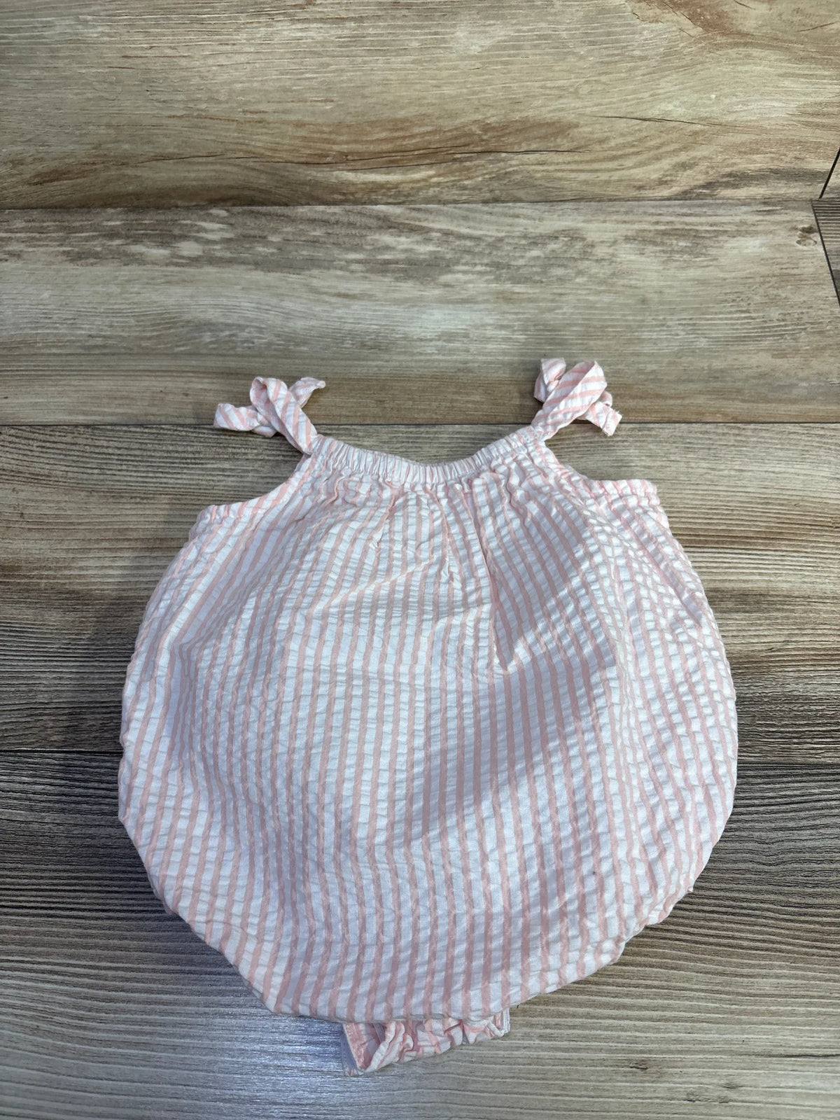 Flat lay of Goodlad pink-and-white striped seersucker romper showcasing tie shoulder straps on a wood-grain background