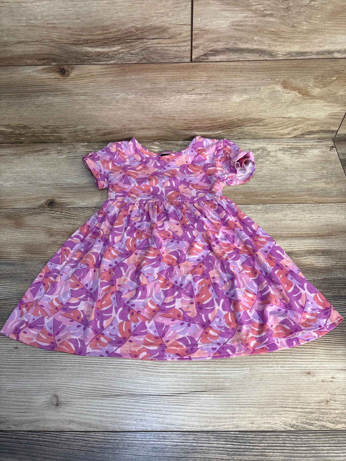 Short sleeve girls' dress with pink and purple leaf print, laid flat on wood floor