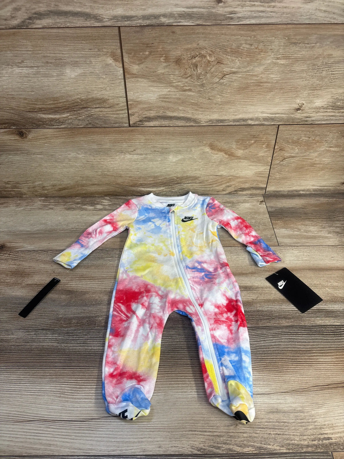 Front view of Nike infant sleeper showcasing multicolor tie dye, long sleeves, footed legs, and front zipper on wood floor