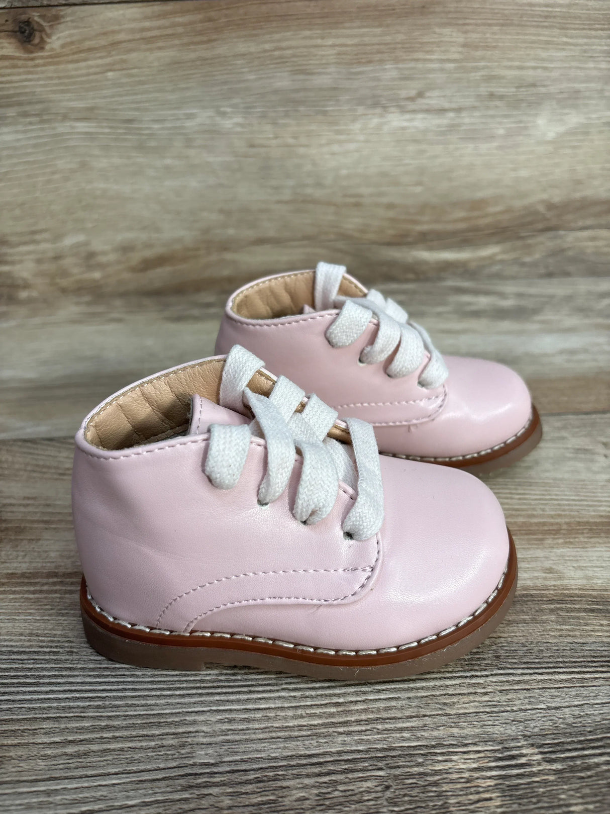 Pair of pink baby leather boots with white laces on wooden surface