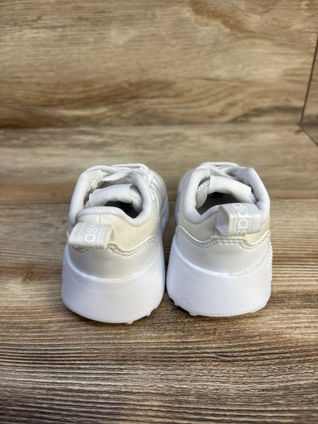White baby sneakers with soft soles and adjustable straps, perfect for first walkers on wooden floor