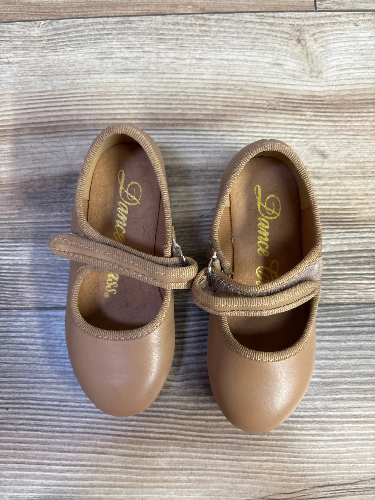 Top view of tan tap shoes in size 7C showing strap closures on a wood-grain background