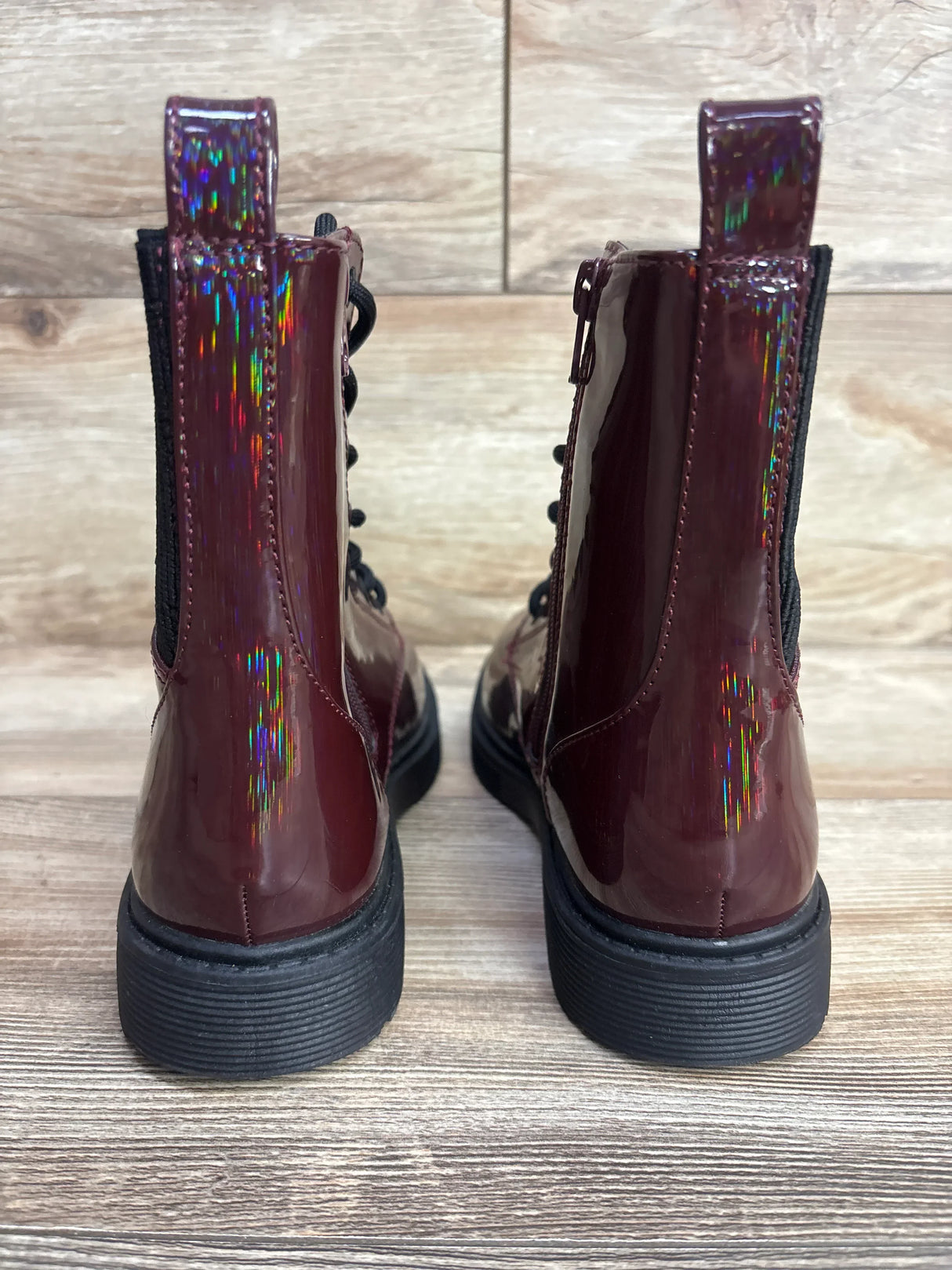 Rear view of shiny maroon kids combat boots with black soles on wood background