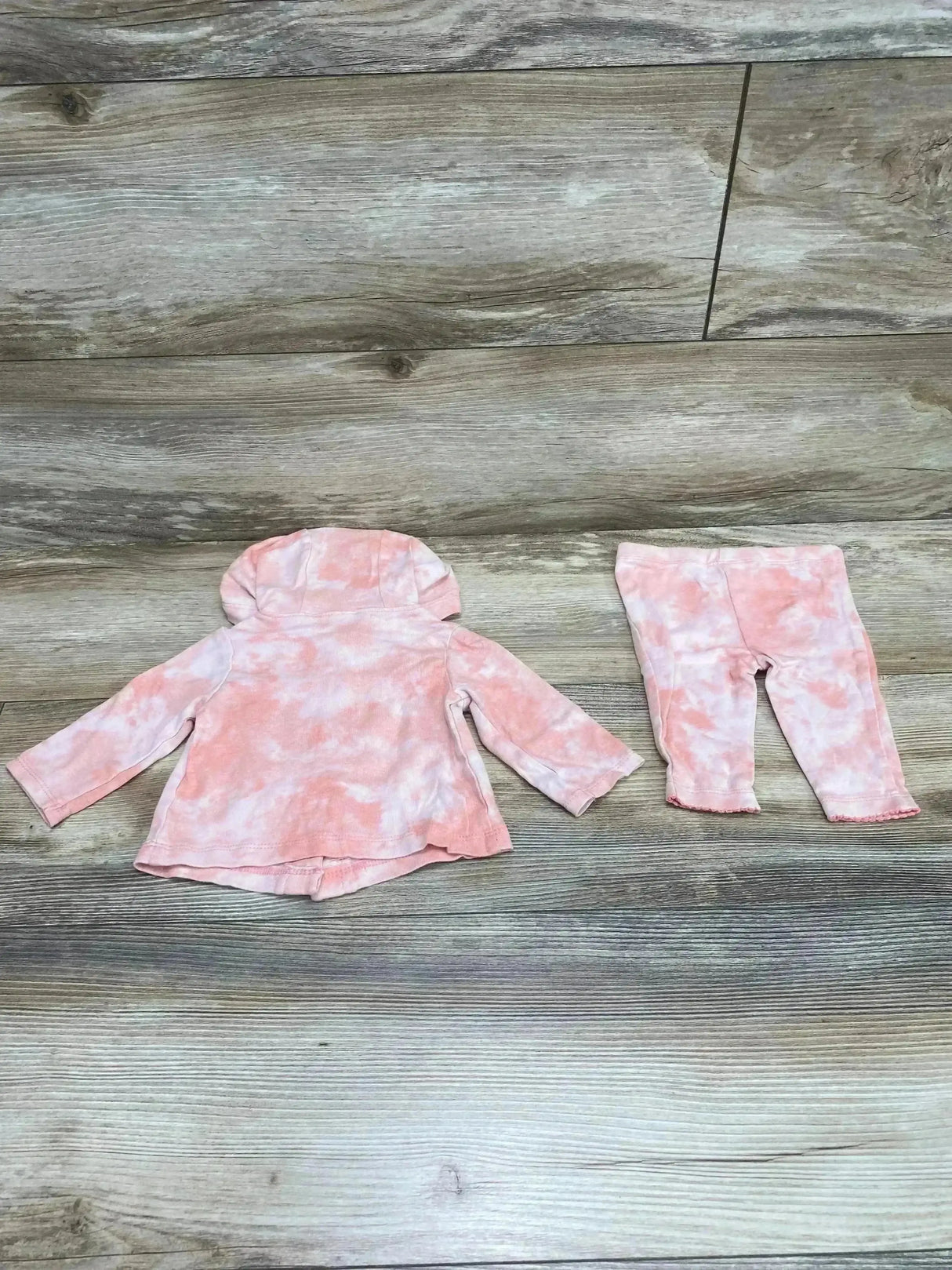Flat lay of Carter’s 2-piece hooded top and leggings showcasing pink tie-dye pattern on wood plank background