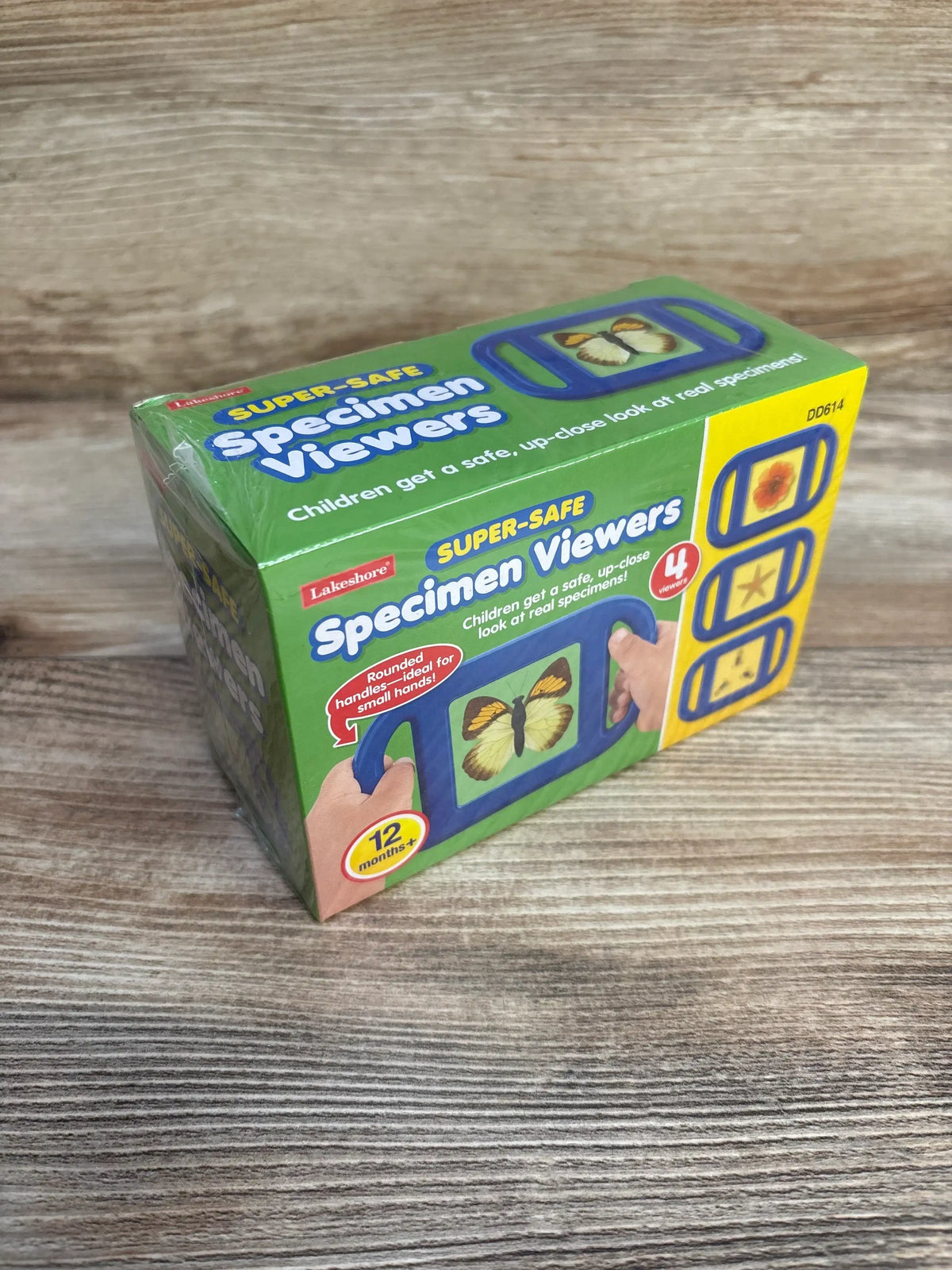 Three-quarter view of Lakeshore Super-Safe Specimen Viewers box showing green packaging with blue viewer illustration, ‘12 months+’ badge, and product images on a wood surface