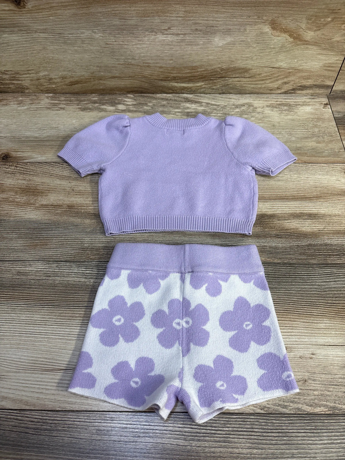 Flat lay of Grayson Mini knit top and shorts set showcasing puff sleeves and purple floral shorts on wood