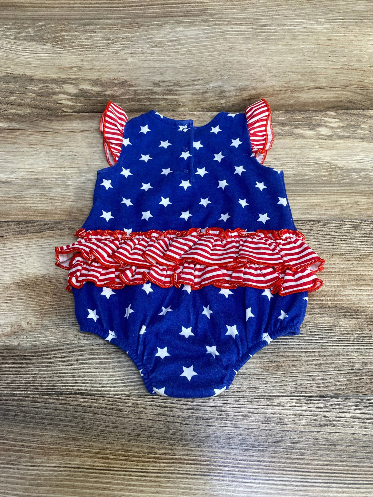 Flat lay of Baby Starters blue stars-and-stripes romper (9 months) showing ruffled striped waist and flutter sleeves on wood background