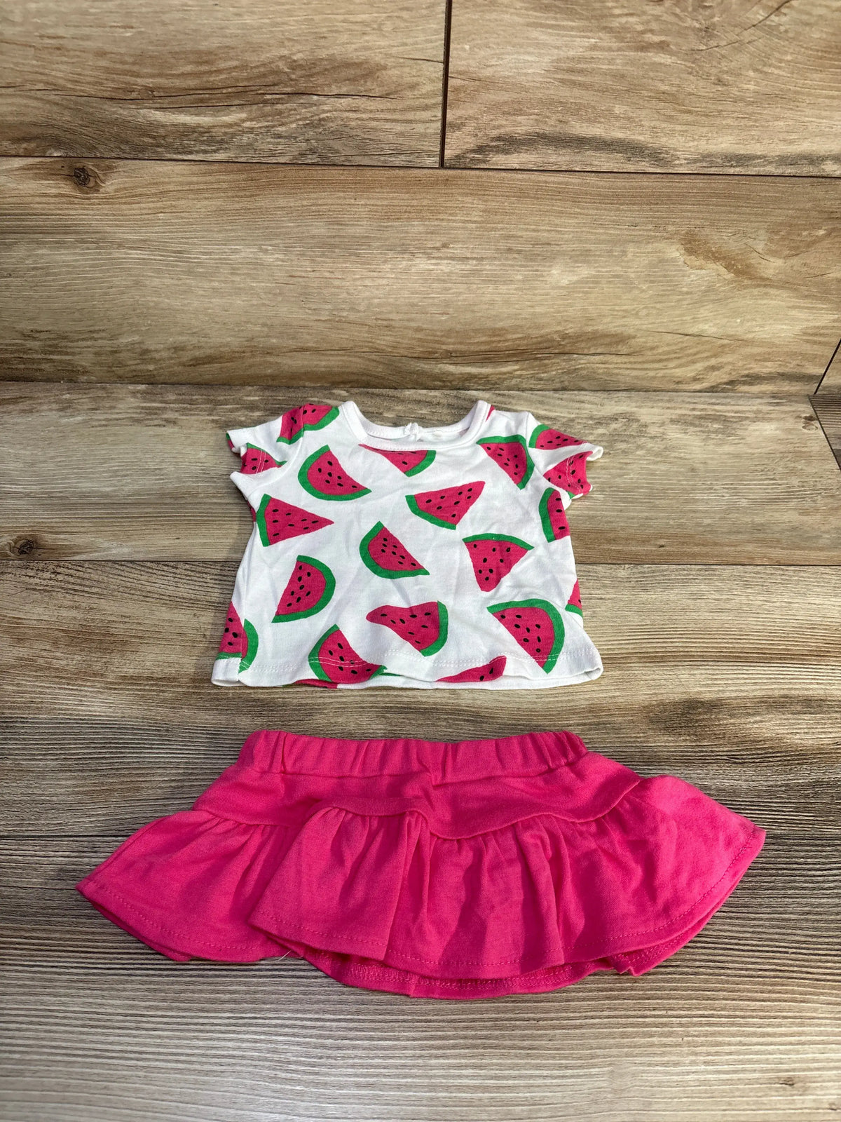 Front view of BWA watermelon shirt and skort set with watermelon print and pink layered skort on wood-patterned background