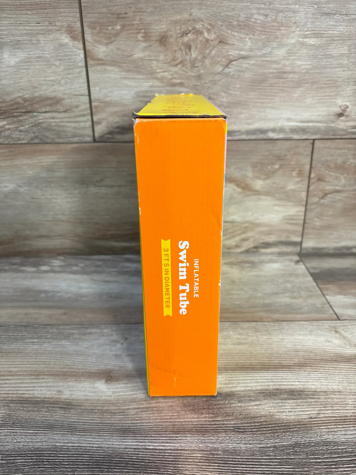 Side of orange box labeled inflatable swim tube 3ft 5in diameter on wood floor