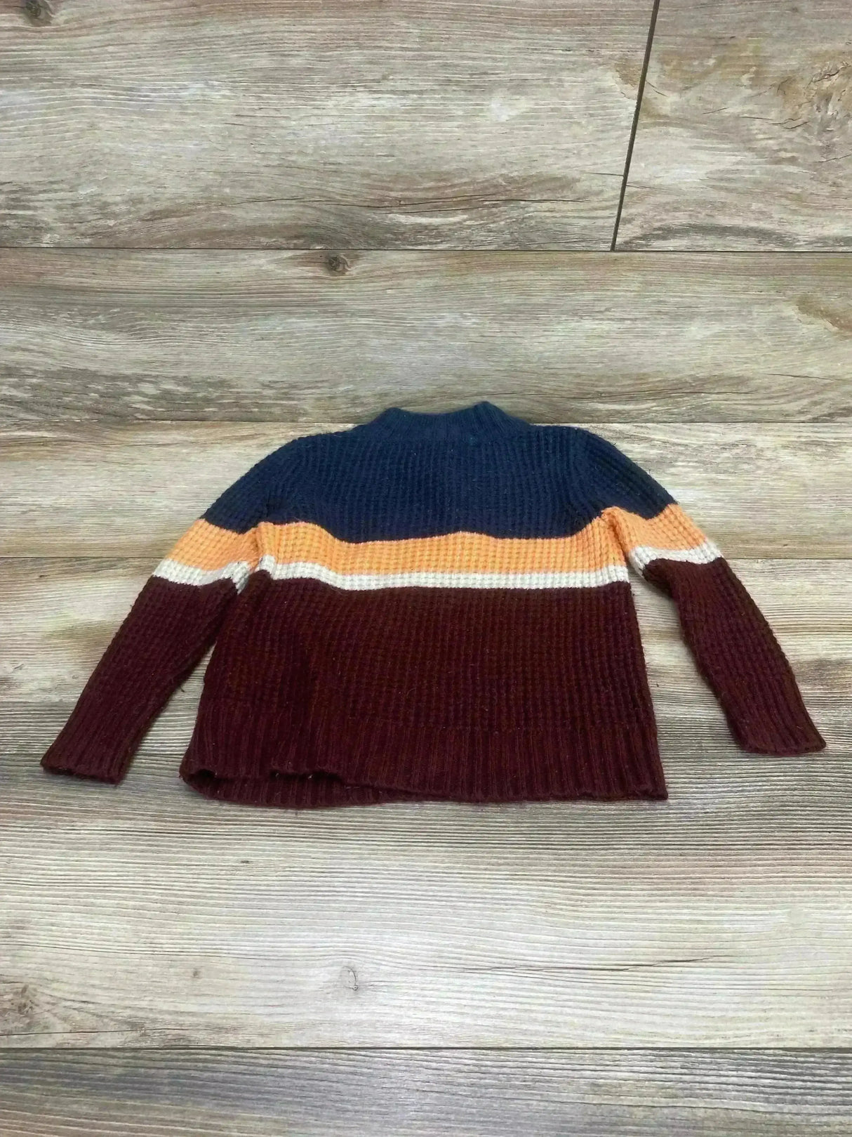 Flat lay of Cat & Jack colorblock knit sweater showing navy yoke, orange and white stripes and burgundy body on wood floor