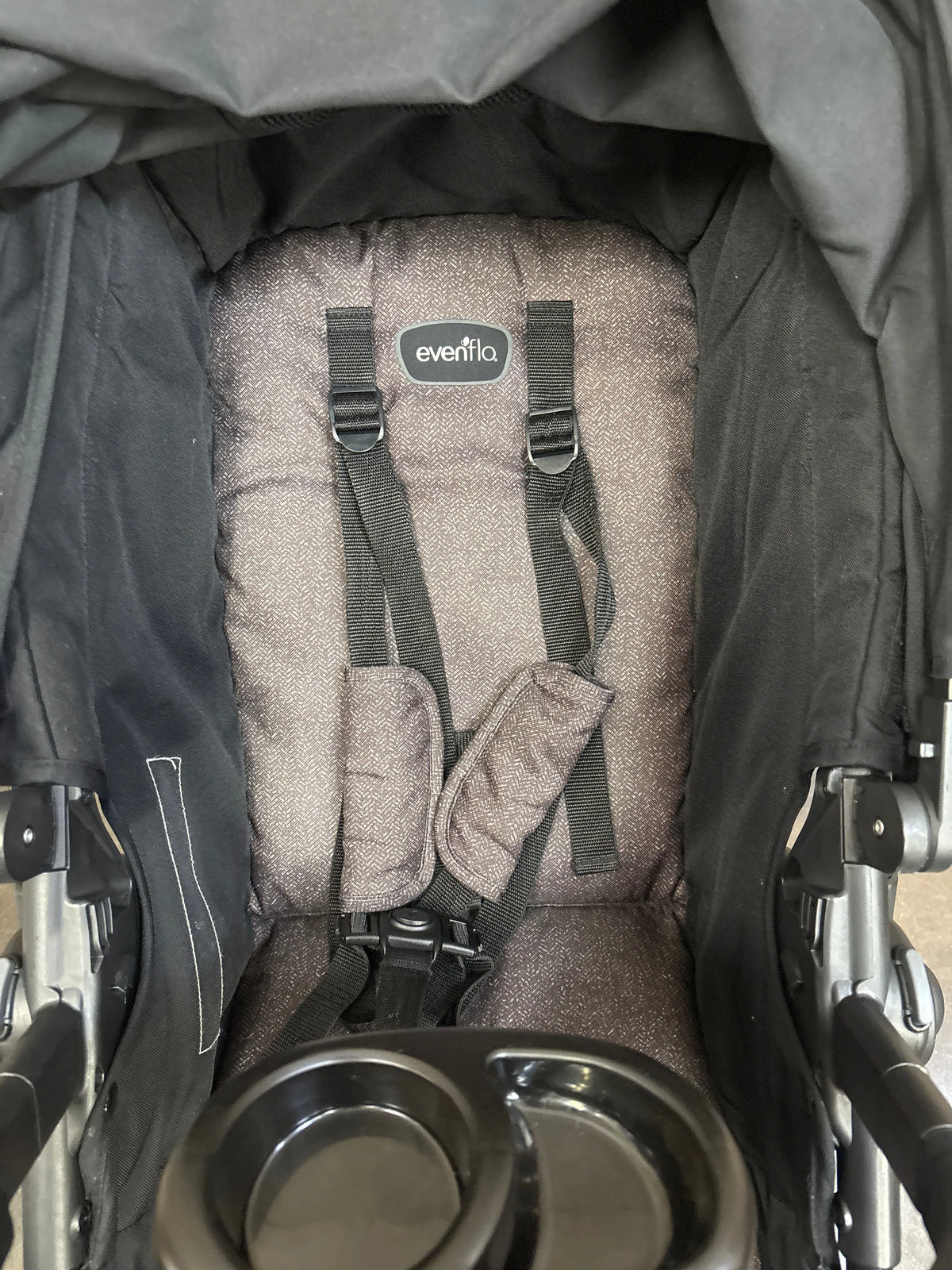 Close-up of Evenflo Pivot stroller showcasing padded seat, five-point harness, and dual cup holder with black frame