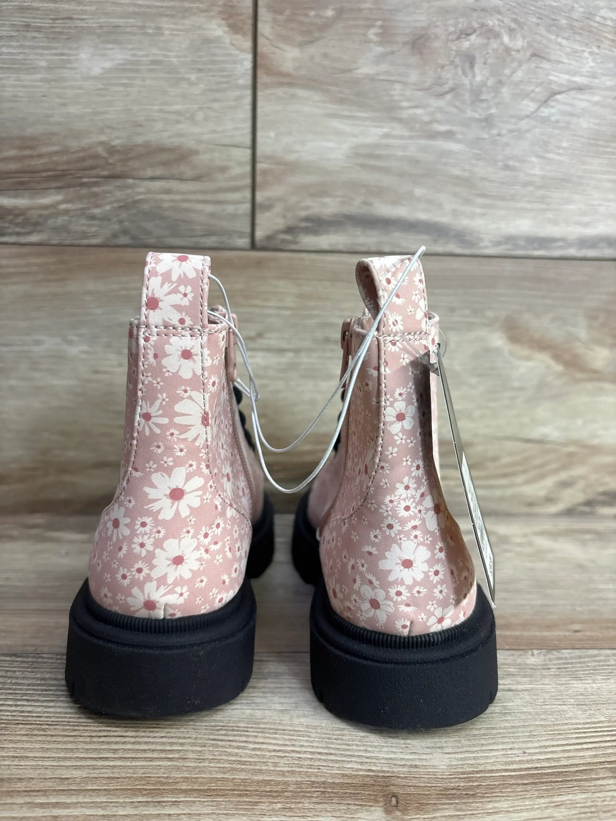 Back view of pink children's boots with white floral pattern and black soles on wood floor