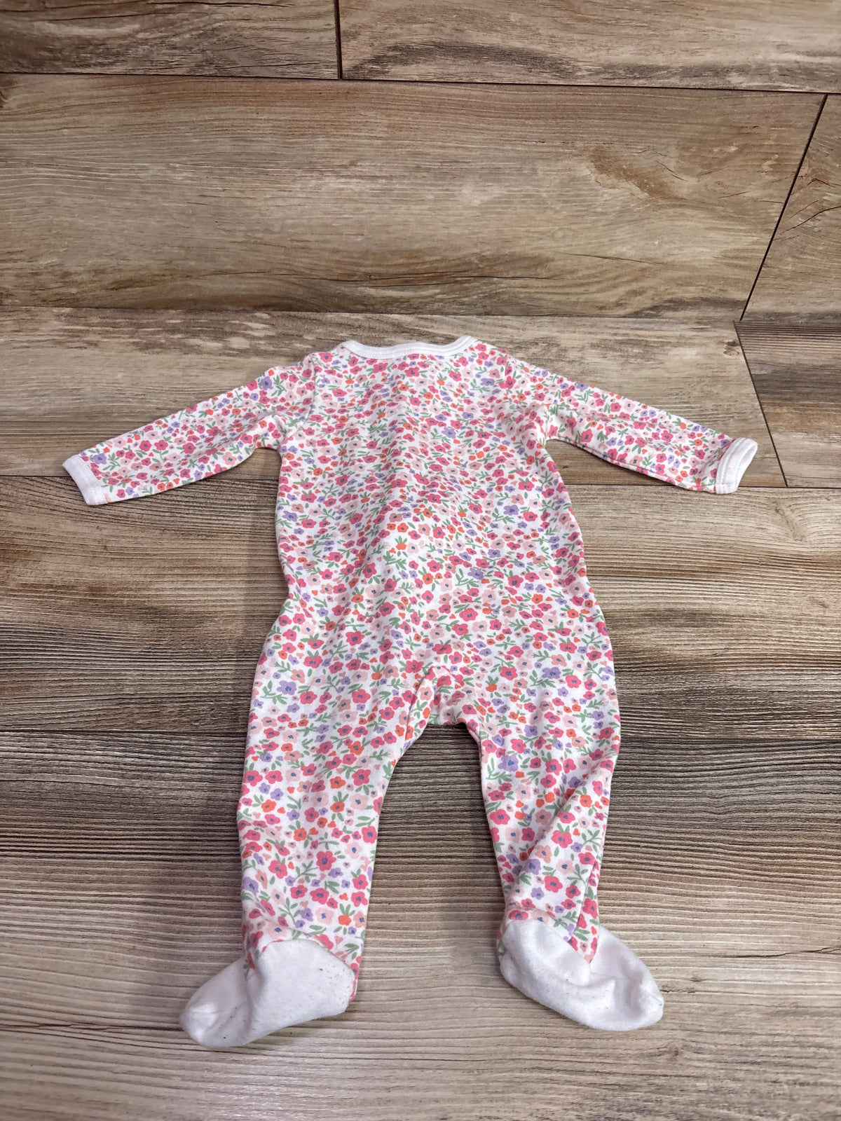 Front view of Mini Hop Sleeper in white with floral print, long sleeves, and built-in feet on a wood background