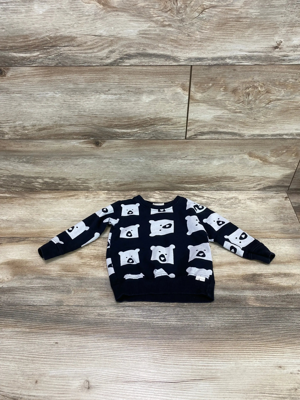 Flat lay of Turtledove London navy toddler sweatshirt 1-2T showing white bear-face print, crewneck and ribbed cuffs on wood