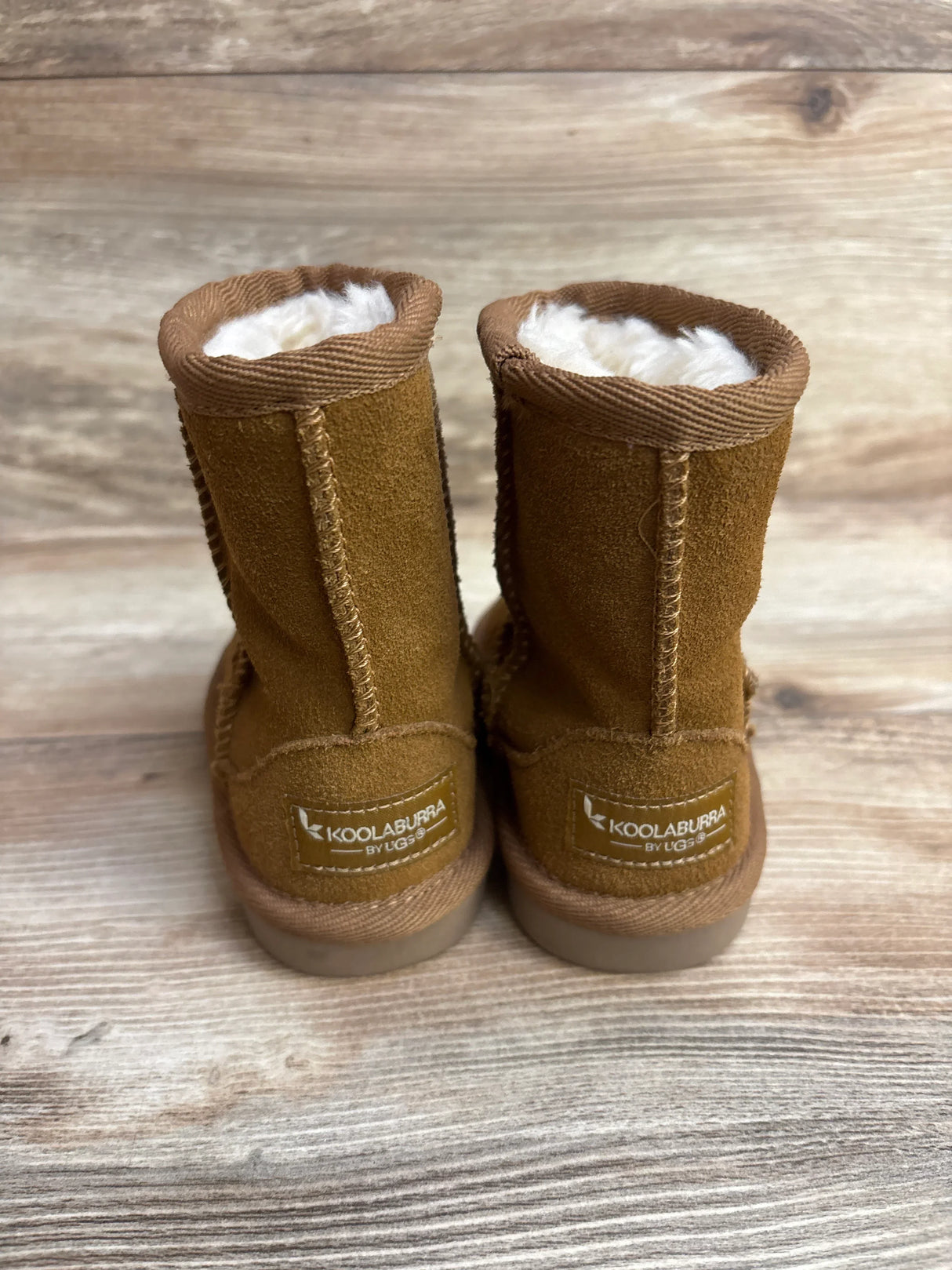 Back view of brown Koolaburra by UGG kids shearling boots on wooden surface