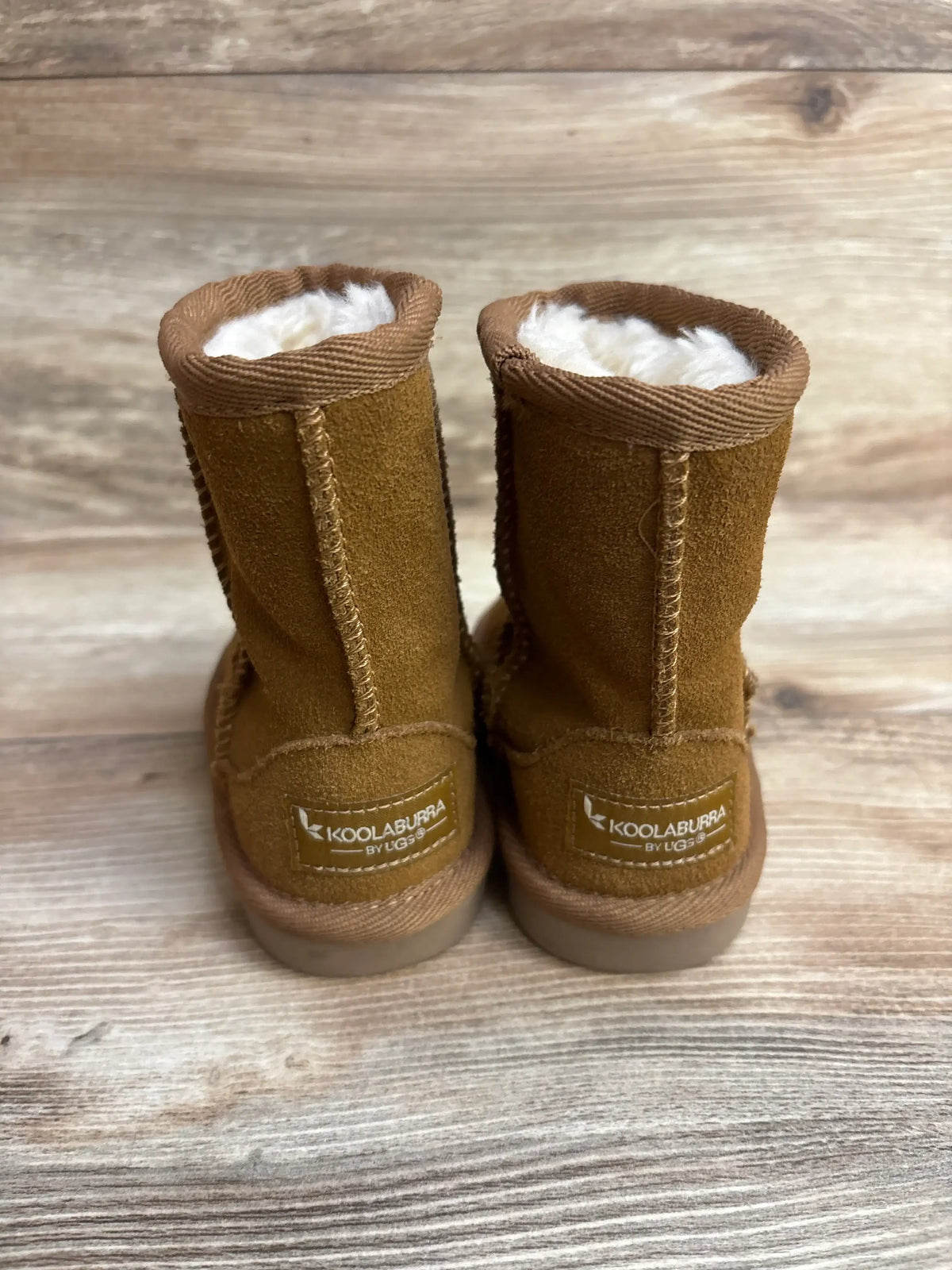 Back view of brown Koolaburra by UGG kids shearling boots on wooden surface