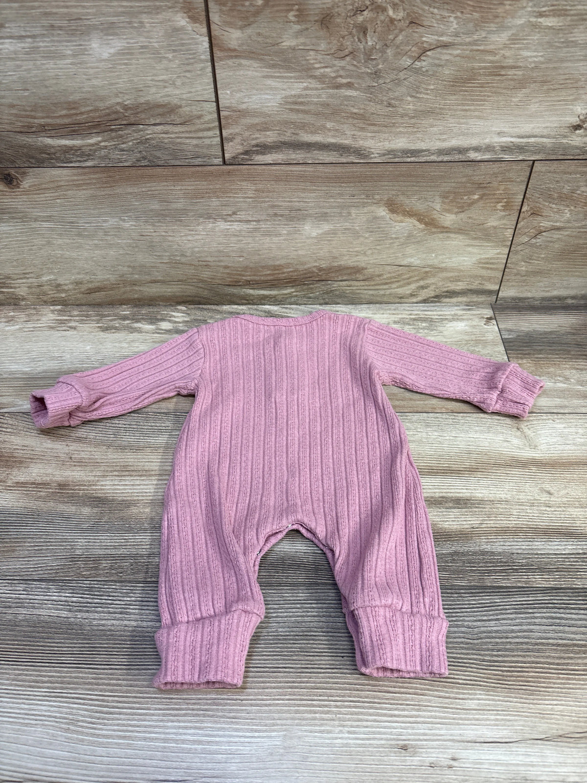 Back view of pink knit Henley coverall in size 3m showcasing ribbed texture and wide cuffs on a wood-look floor