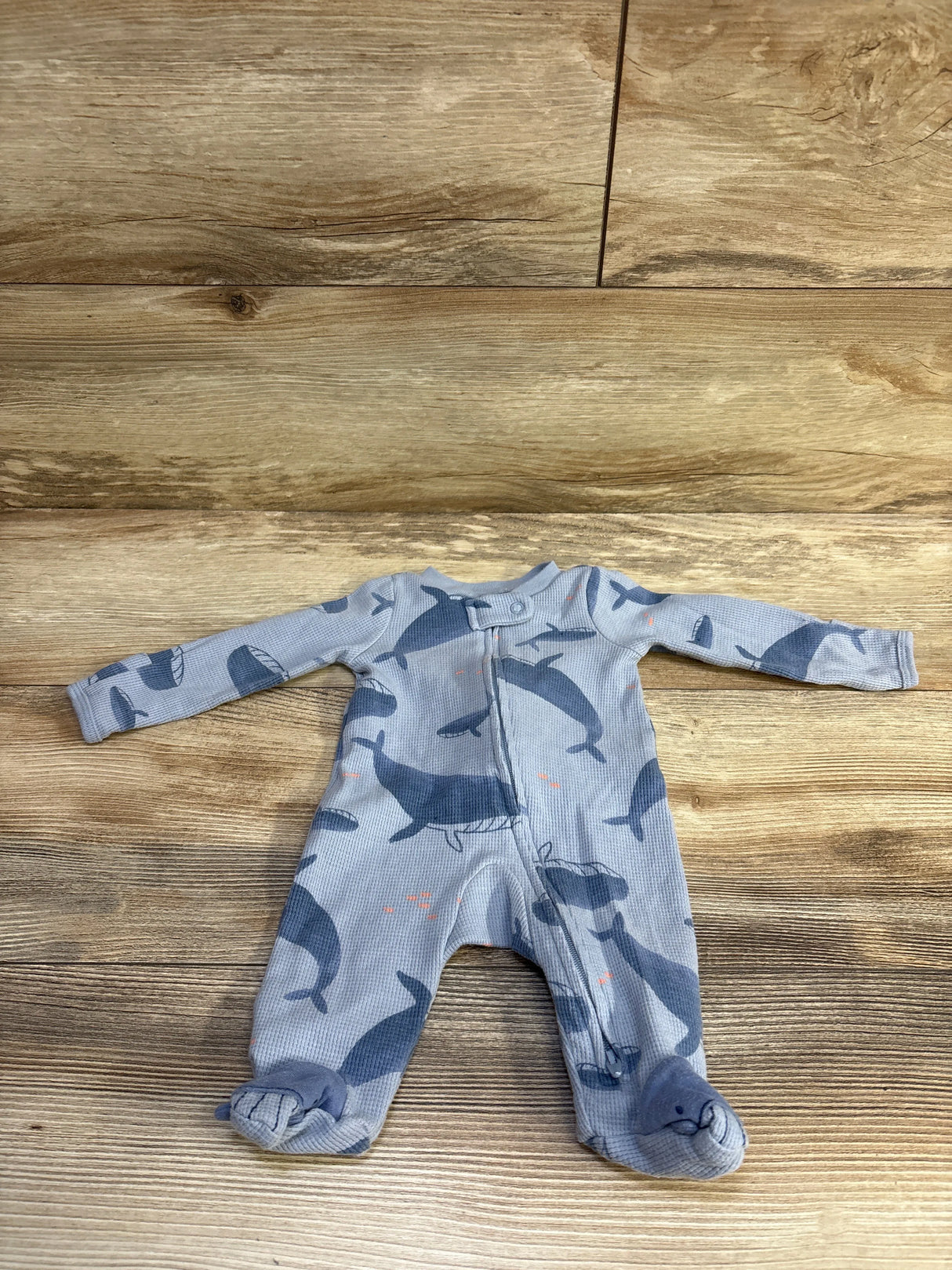 Front view of Just One You newborn waffle knit footed sleeper in light blue with navy whale print and front zipper on wood
