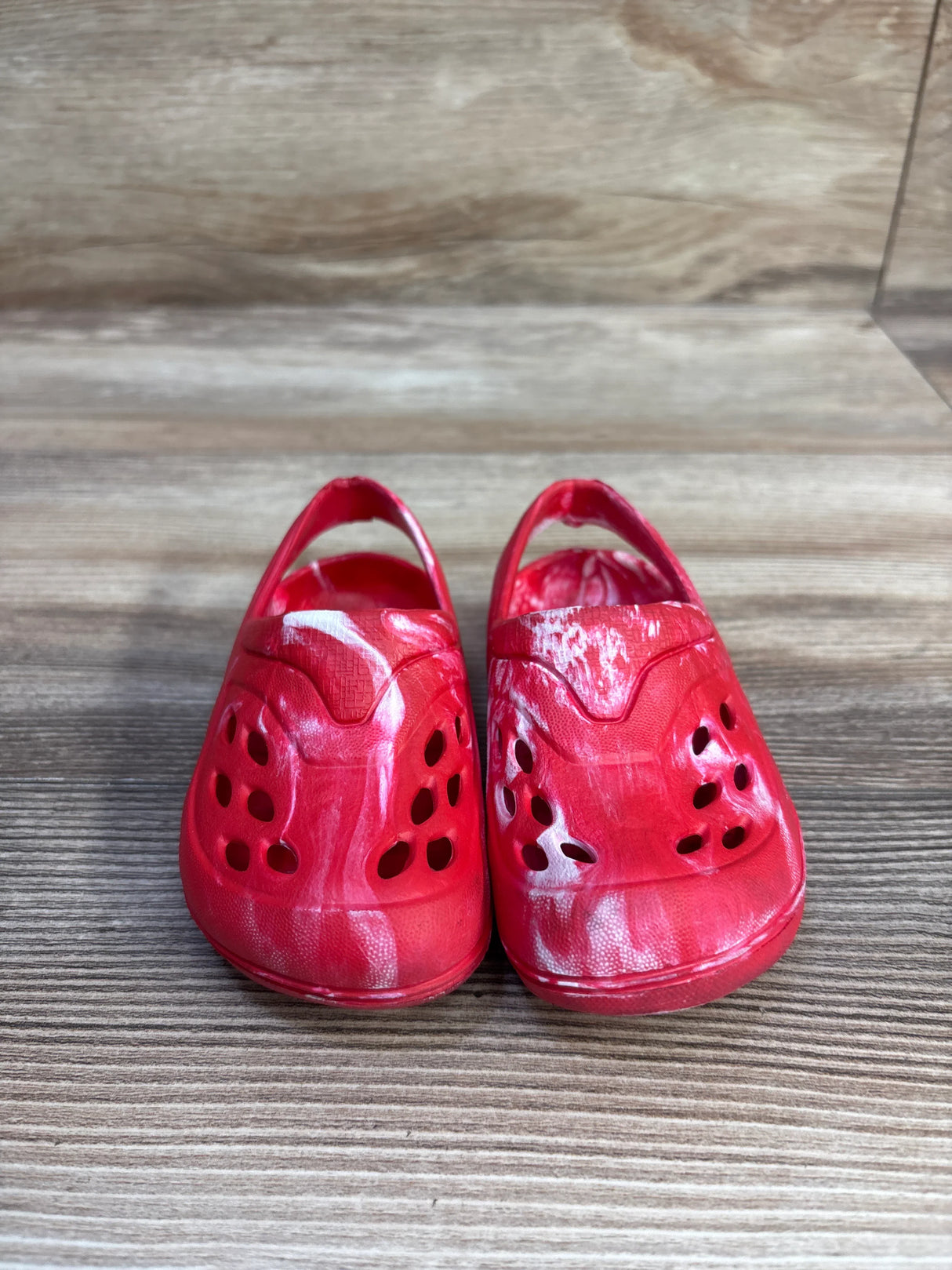 Front view of Wonder Nation toddler red tie-dye clogs showing ventilation holes, back straps, and white swirl pattern on wood surface