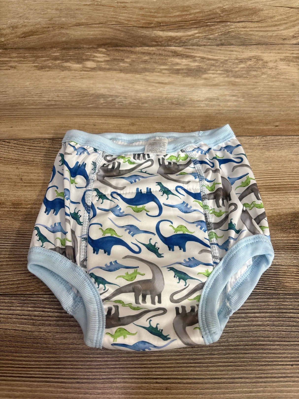 Front view of EZ Moms 5T potty-training underwear showing double-absorption panel and blue dinosaur print on wood background
