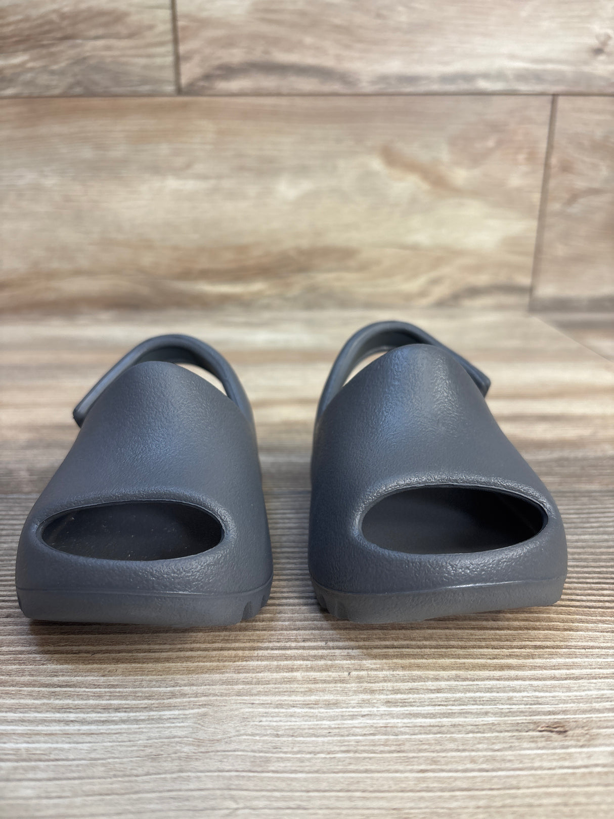 Front view of Adidas Yeezy Slides in Granit, kids size 3C, showing open-toe design and back strap on wood floor
