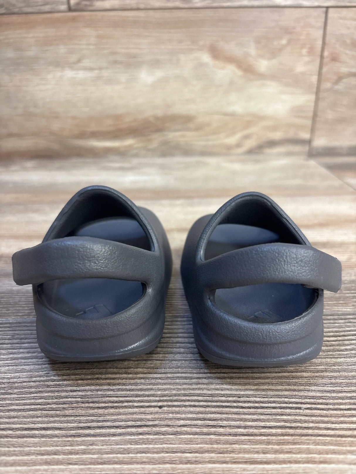 Back view of Adidas Yeezy Slides in Granit, kids size 3C, showing heel strap and contoured footbed on wood floor