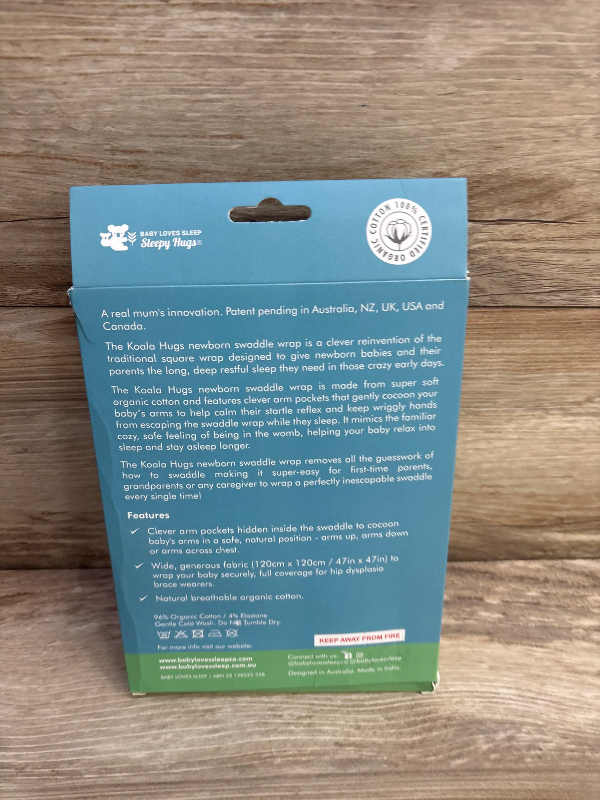Back of Baby Loves Sleep Koala Hugs newborn swaddle teal packaging with product features text on wood