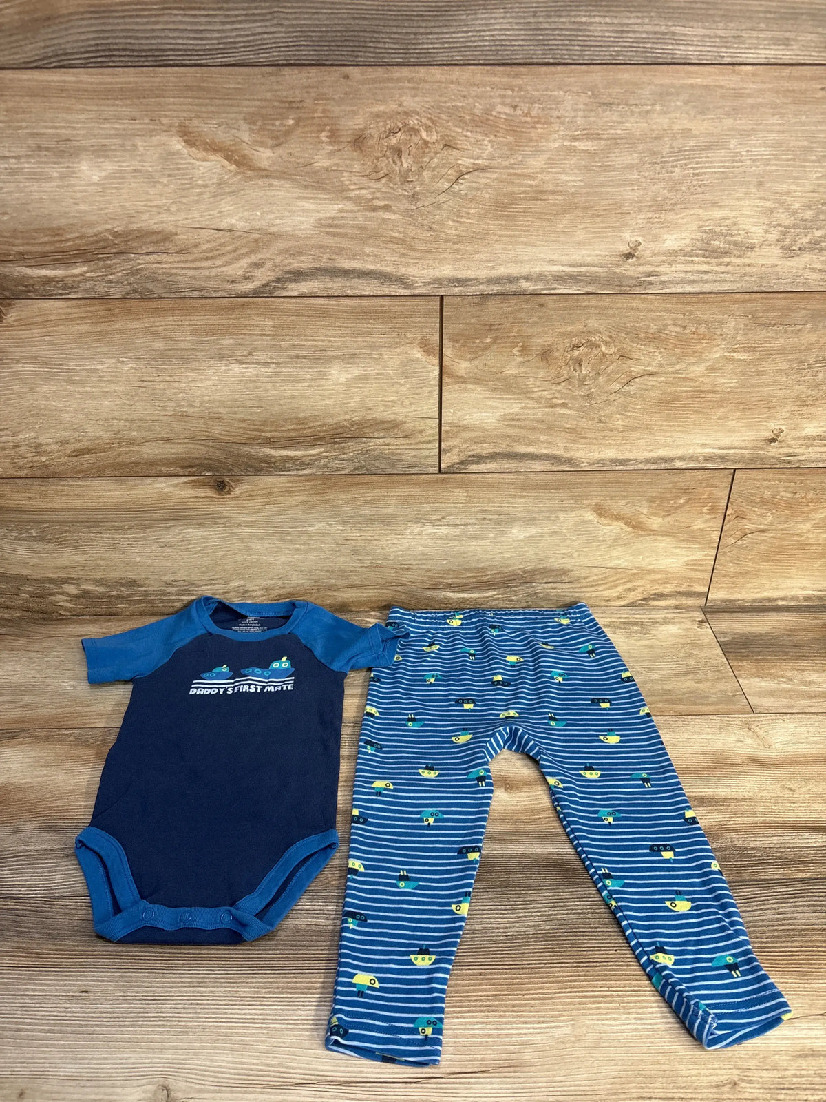 Front view of Okie Dokie blue Daddy’s First Mate bodysuit and pants set with submarine-patterned pants on wood background
