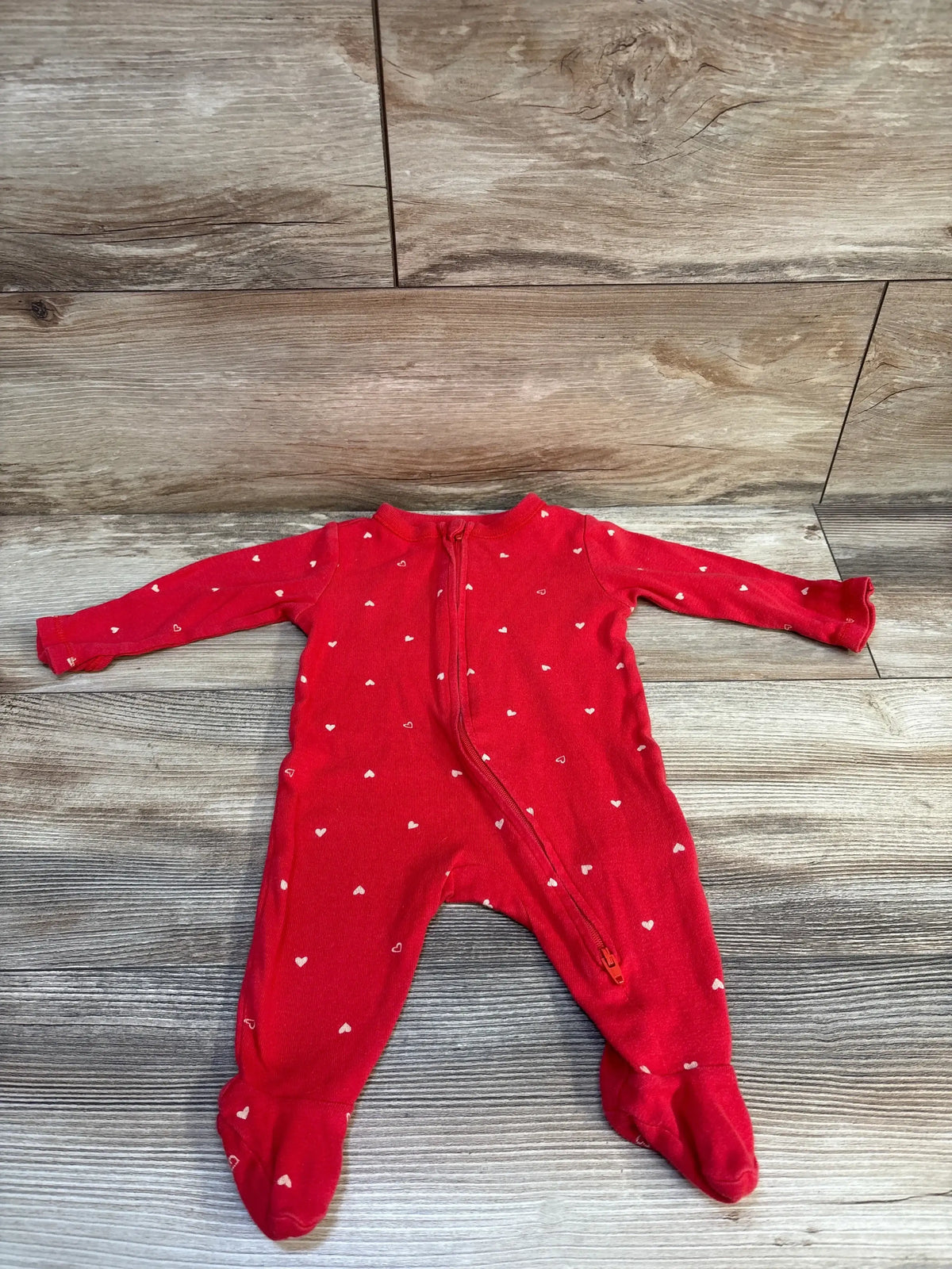 Red baby footed sleeper with white heart print and front zipper on wooden background