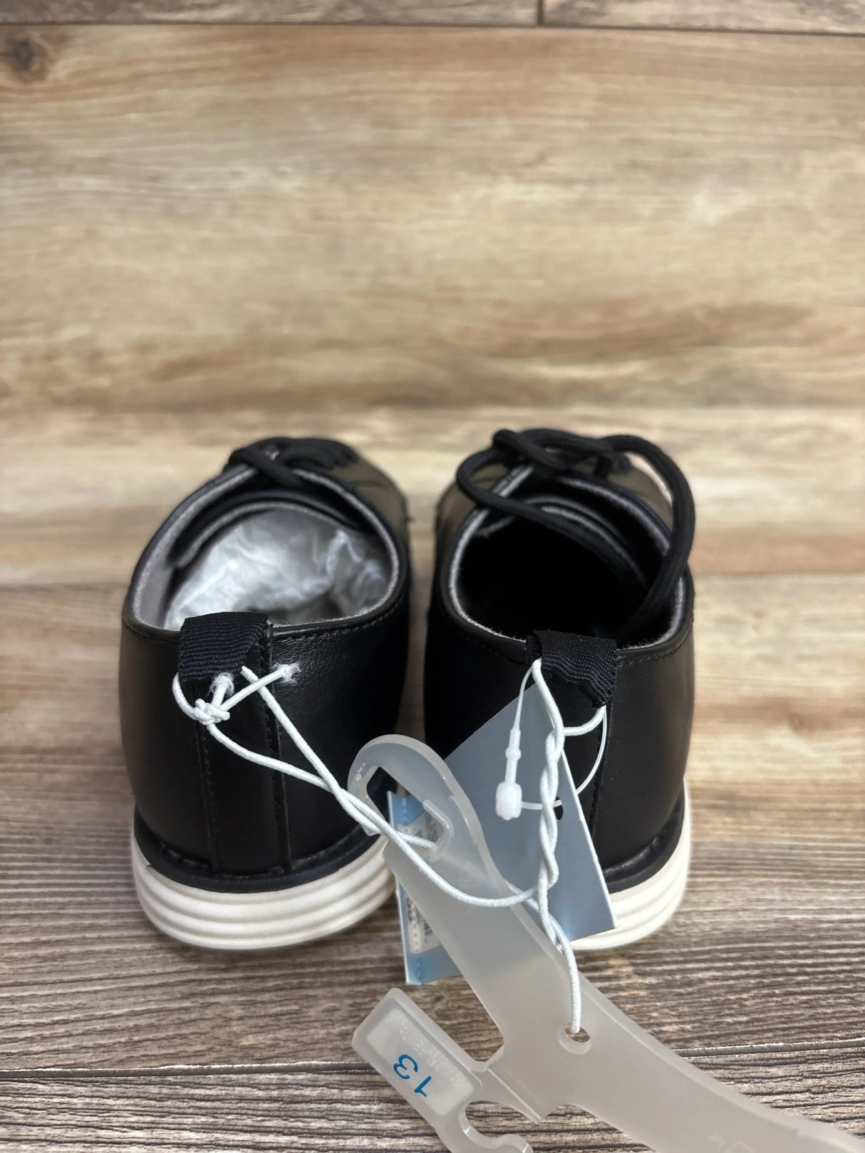 Rear view of Cat & Jack Alfi toddler dress shoes in black showcasing white soles and attached size 13 tag on wooden floor