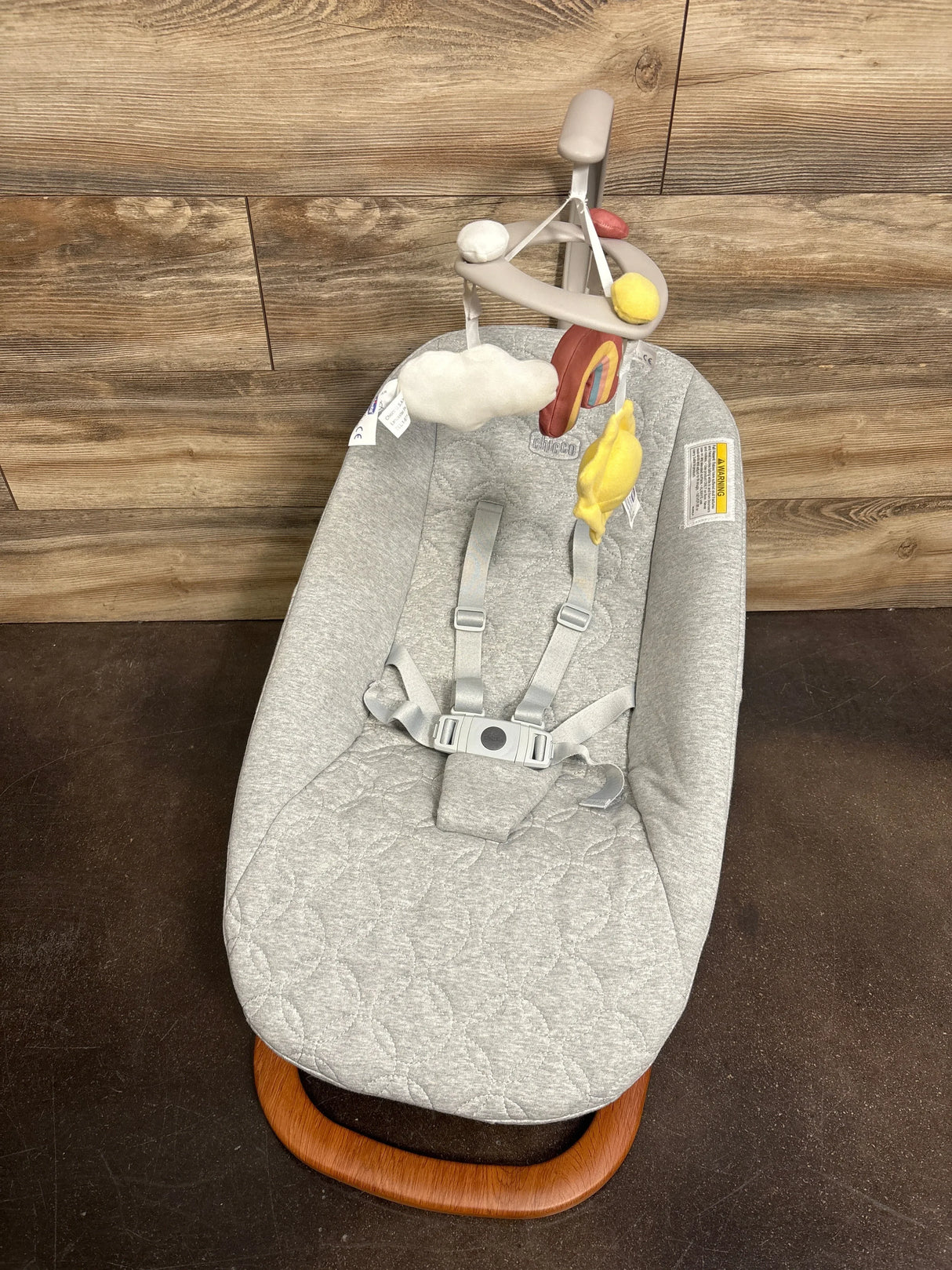 Top view of Chicco Float baby seat with light-gray quilted cover, adjustable straps, hanging cloud and sun toys, wood base