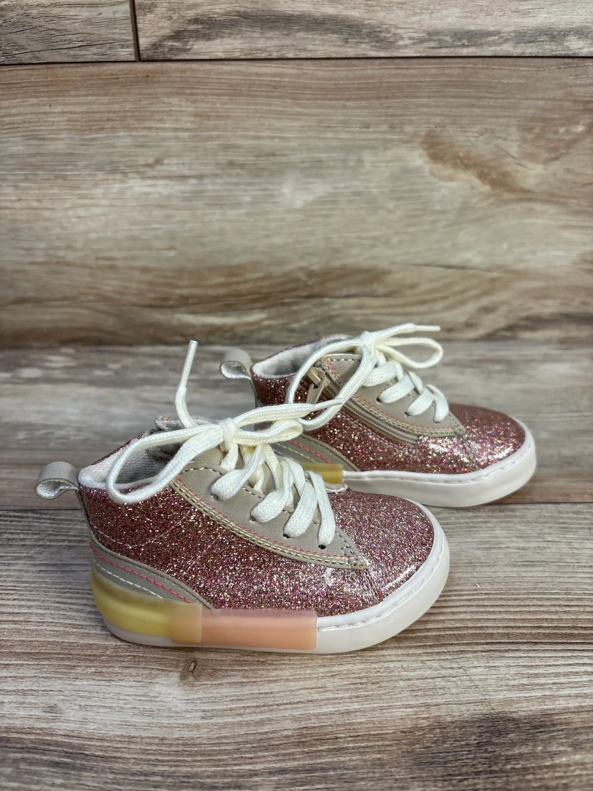 Three-quarter view of Zara pink glittery high-top sneakers showcasing white laces, side zippers, and pull tabs on a wood surface