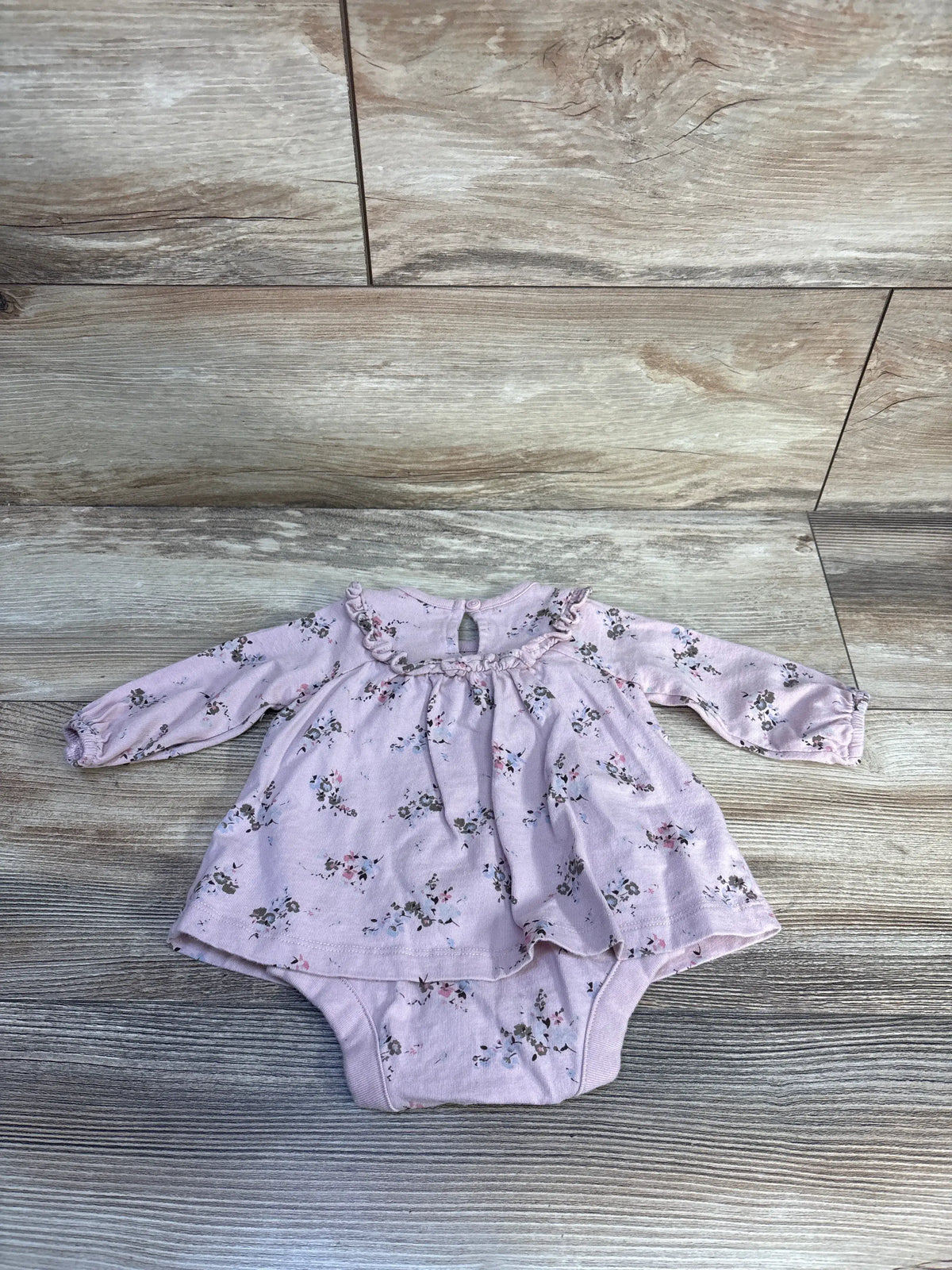 Front view of Baby Gap pink bodysuit dress showcasing floral print, ruffled round neckline, and long sleeves on a wood-look floor