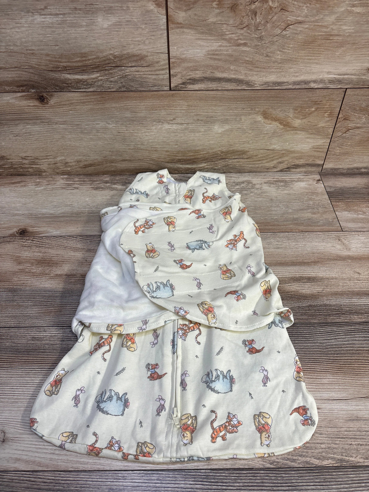 Top-down view of Halo x Disney newborn SleepSack with front zipper, swaddle wings, and Winnie the Pooh print on wood background