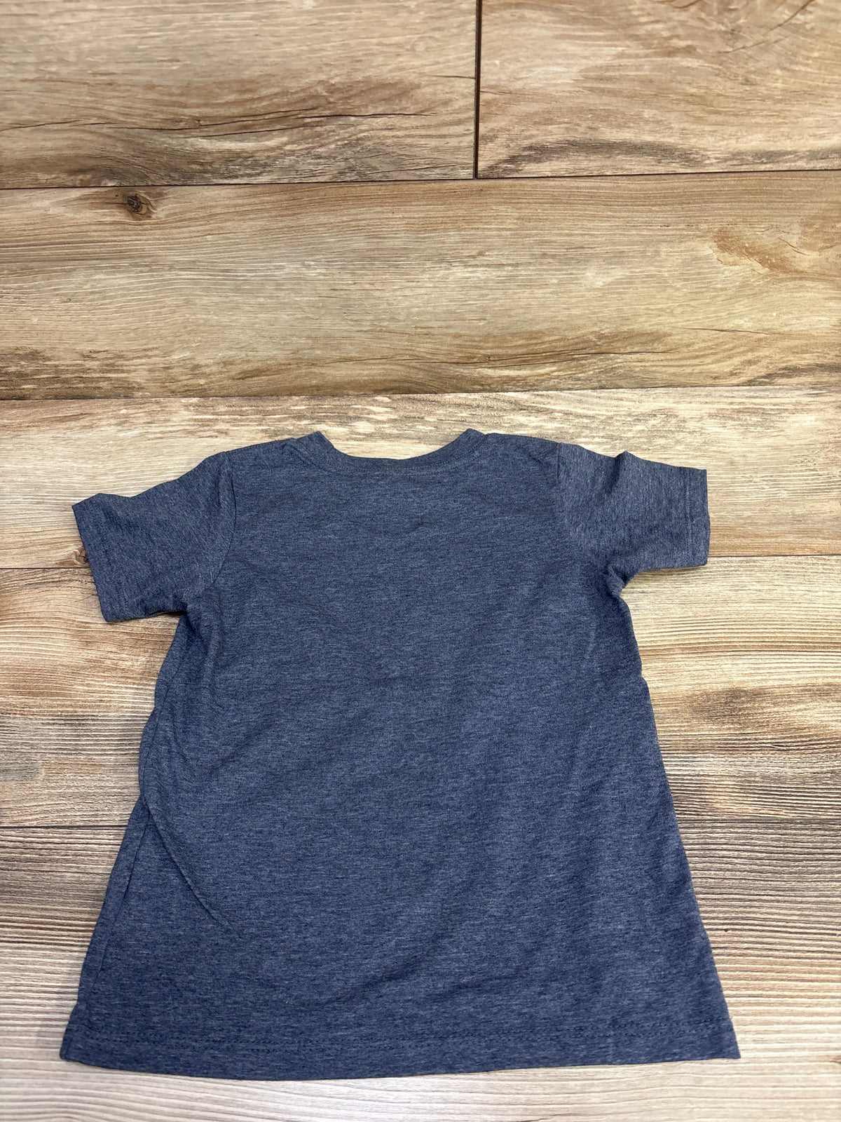Back view of a blue short-sleeve shirt in size 4T laid flat on a wood floor