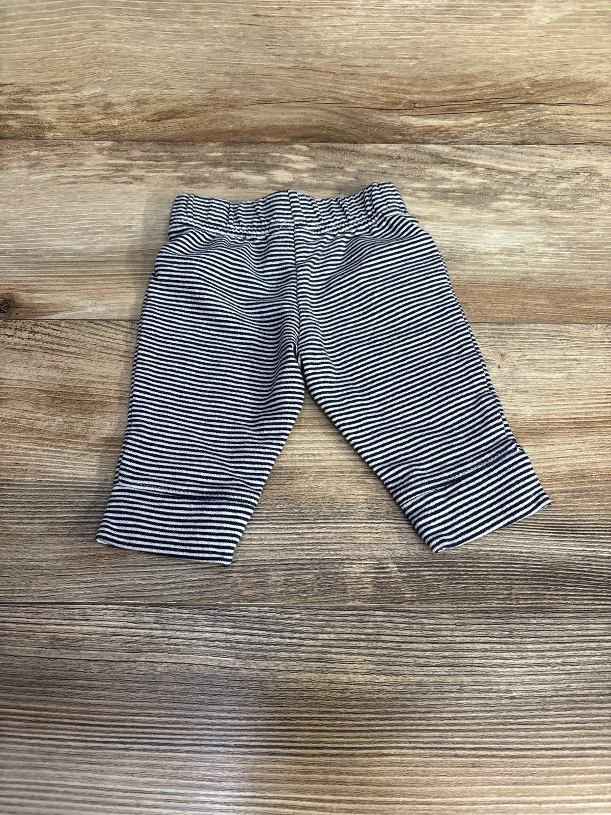Flat-lay front of navy and white striped baby pants size 3M showing elastic waistband and soft knit on light wood background