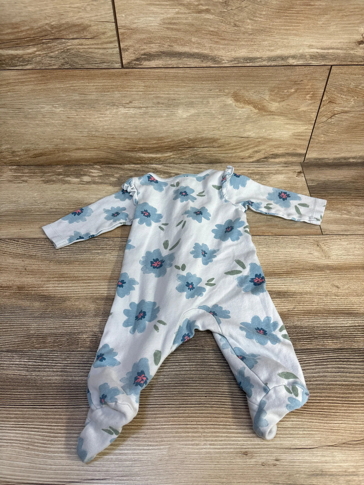 Front view of Just One You blue floral sleeper showcasing long sleeves and footed legs on a wood floor