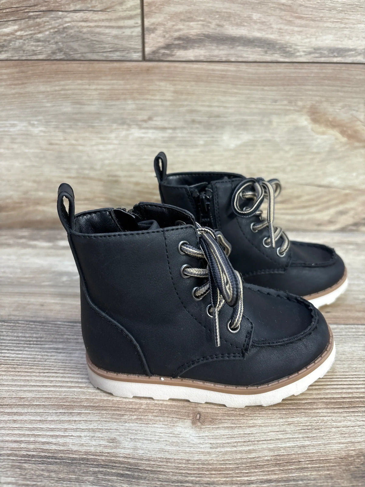 Front three-quarter view of Cat and Jack Greyson black boots showcasing bungee laces and hook and loop Velcro closure on a wood grain background
