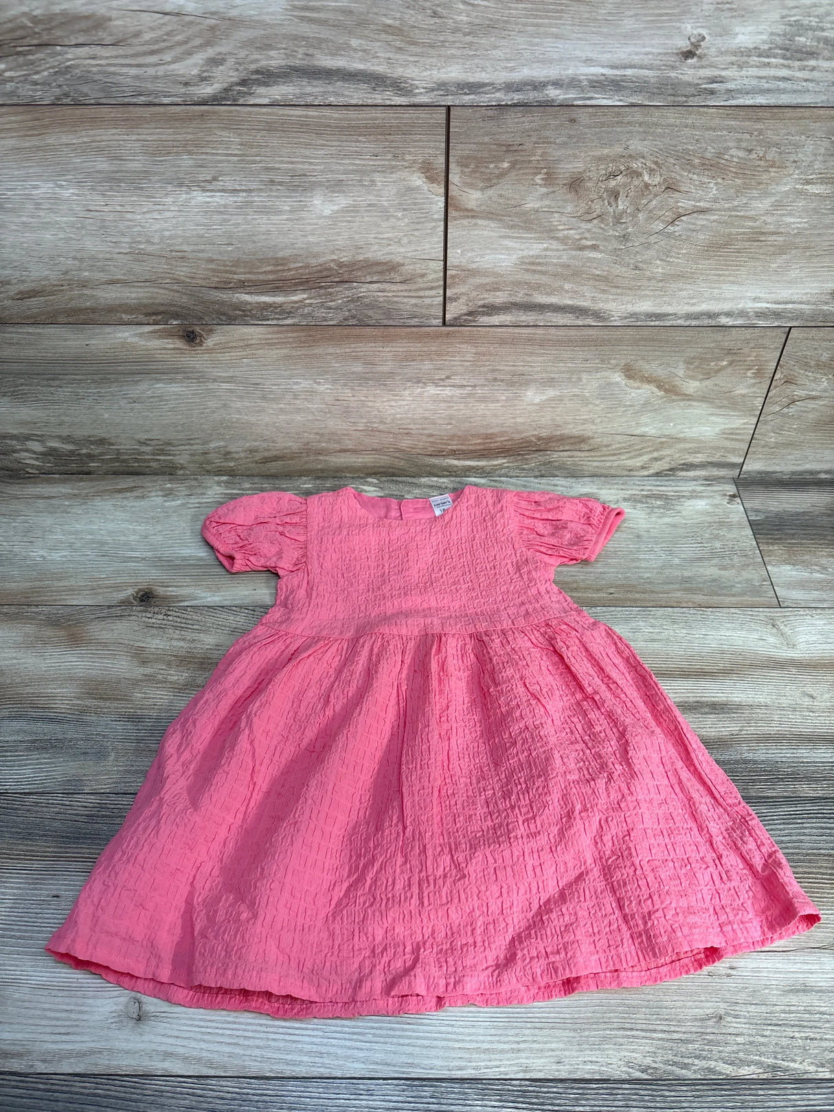 Pink toddler dress with short sleeves on wood background, textured cotton baby dress