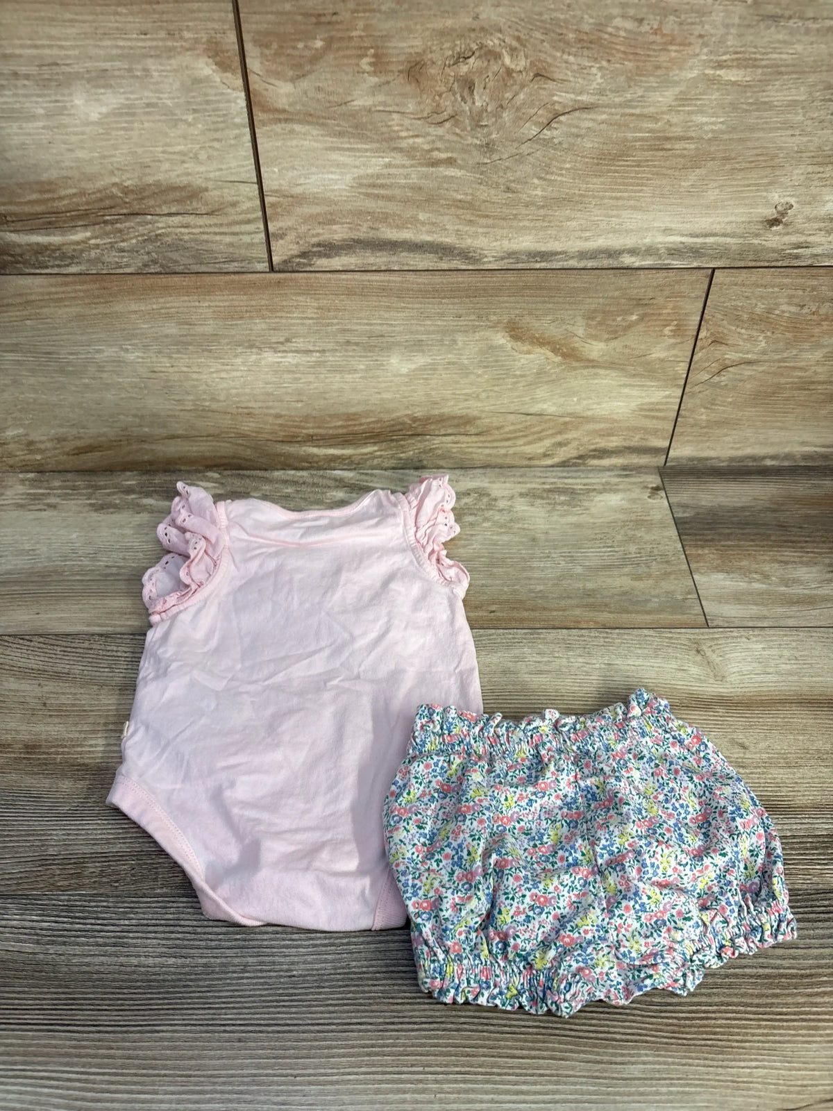 Flat lay of Baby Gap pink two piece bodysuit and floral shorts set showcasing ruffled shoulders on a wood background