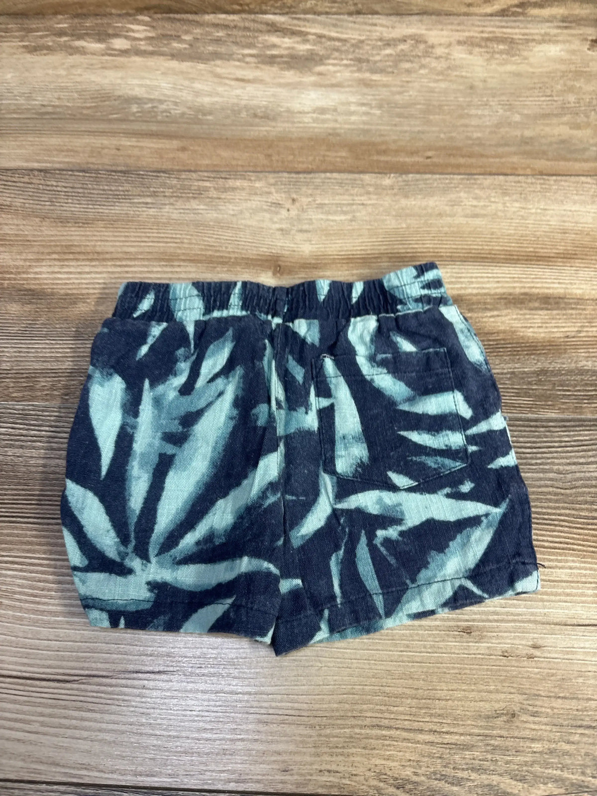 Flat lay of DKNY pull-on linen-blend toddler shorts showcasing elastic waistband and blue leaf print with wood background