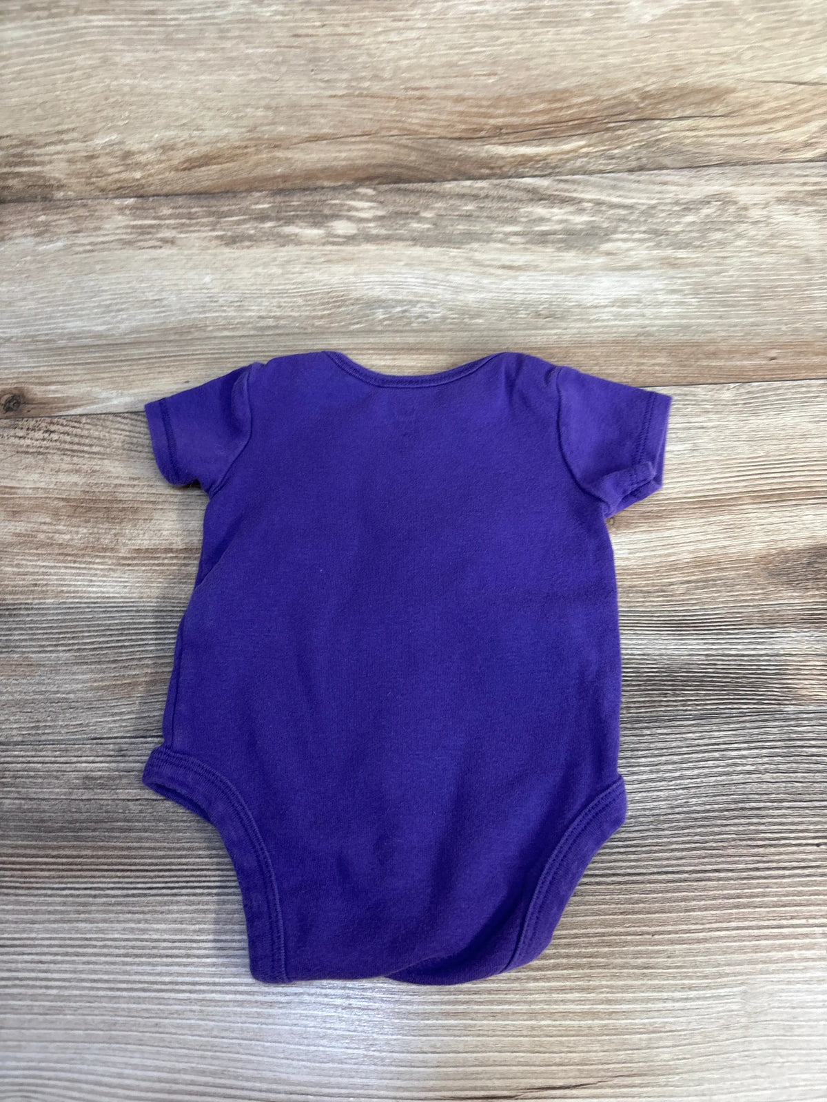 Flat lay of NFL Vikings baby bodysuit in teal and purple showcasing short sleeves on a wood grain background