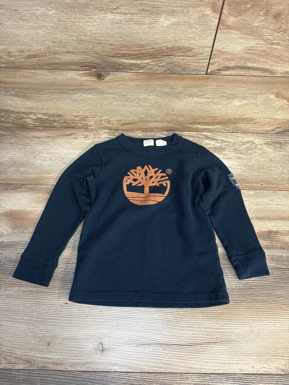 Flat-lay of Timberland navy waffle-knit long-sleeve shirt, size 5T, showing orange tree logo on chest on wood floor
