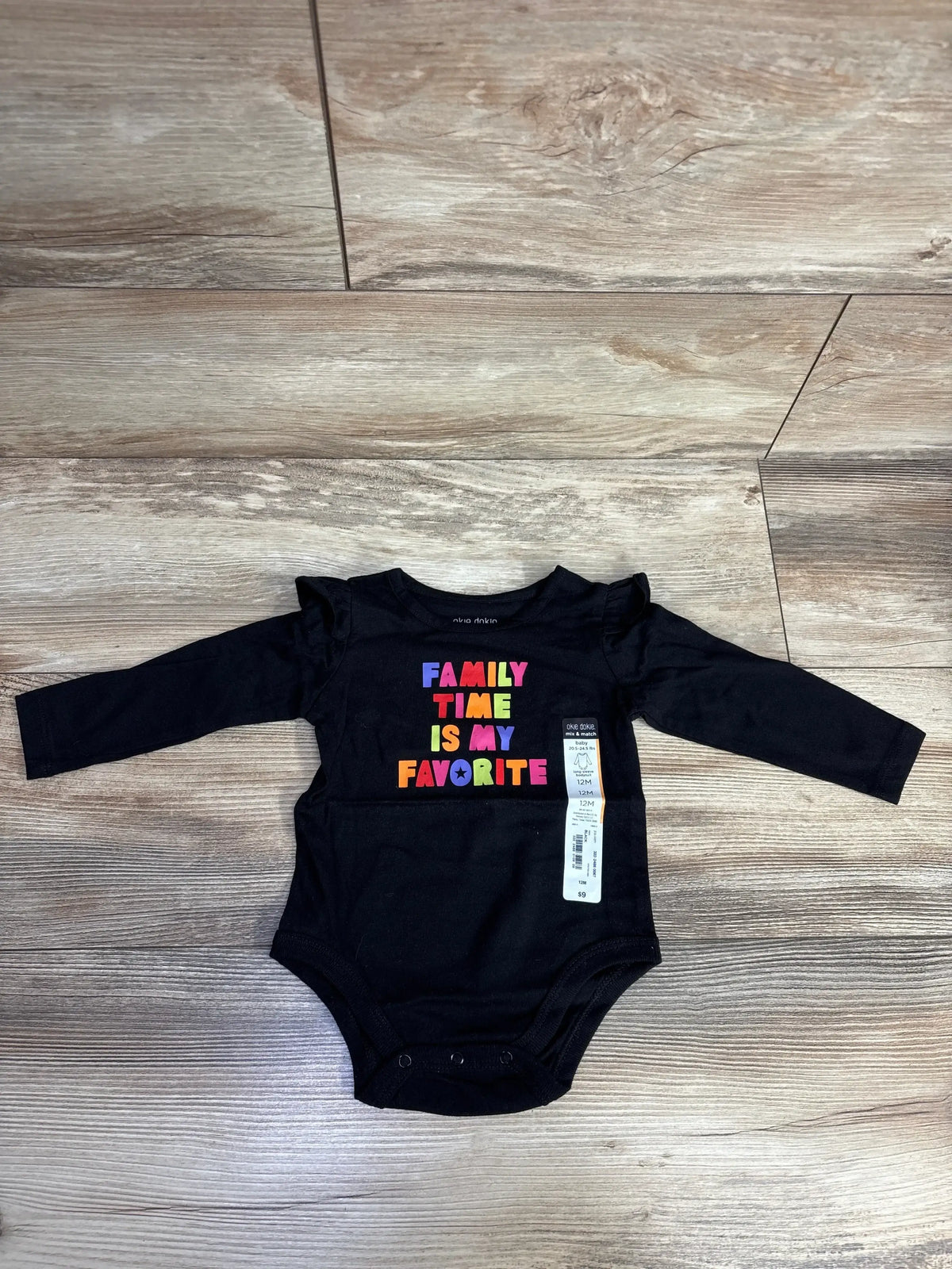 Black long-sleeve baby bodysuit with colorful text reading Family Time Is My Favorite, laid on wooden floor