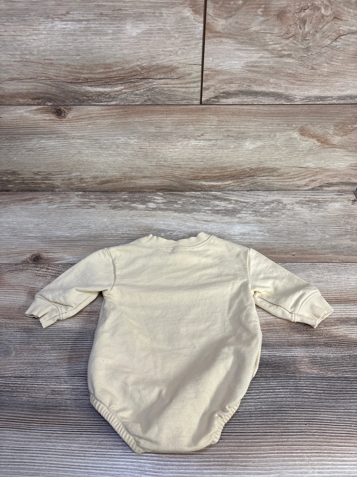 Back view flat lay of yellow bubble romper showing long sleeves and elasticized leg openings on wood background