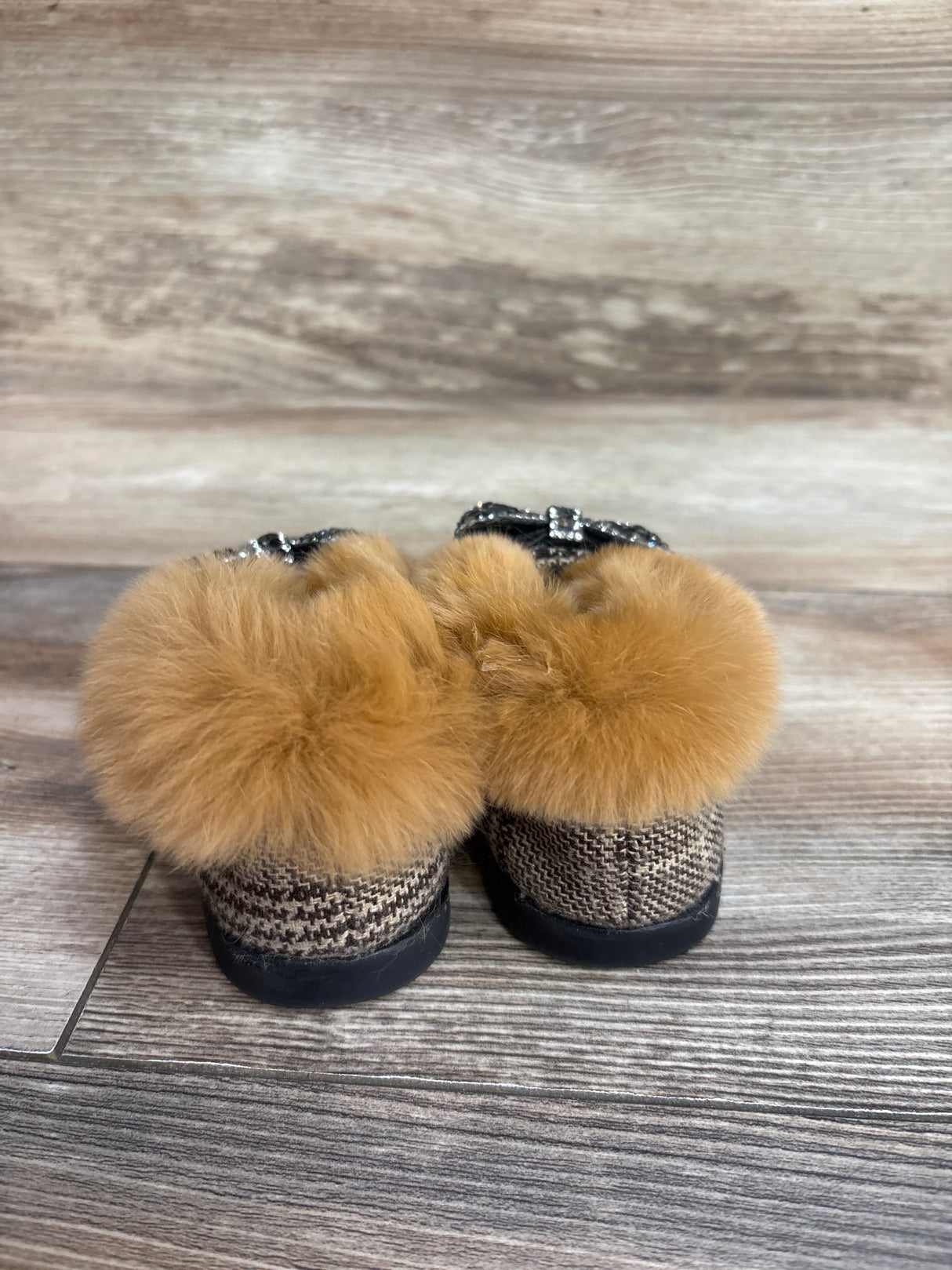 Plaid baby shoes with brown fur trim on wood floor background